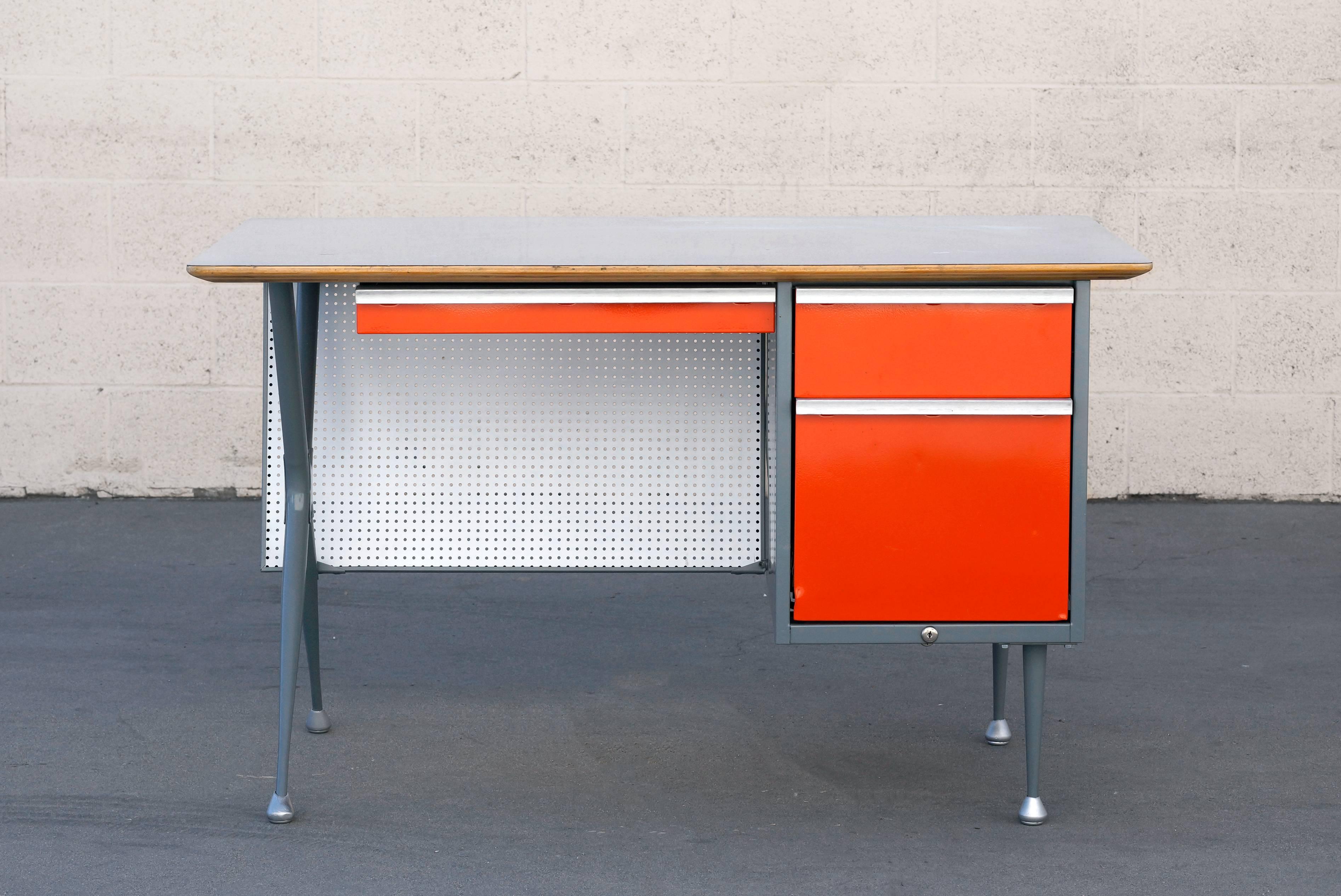 Fantastic 1950s desk by celebrated industrial designer Raymond Loewy desk for Chicago manufacturer Brunswick. We restored this beauty with powder coated light gray frame and orange drawers. Features unique pegboard modesty panel, aluminum trim and