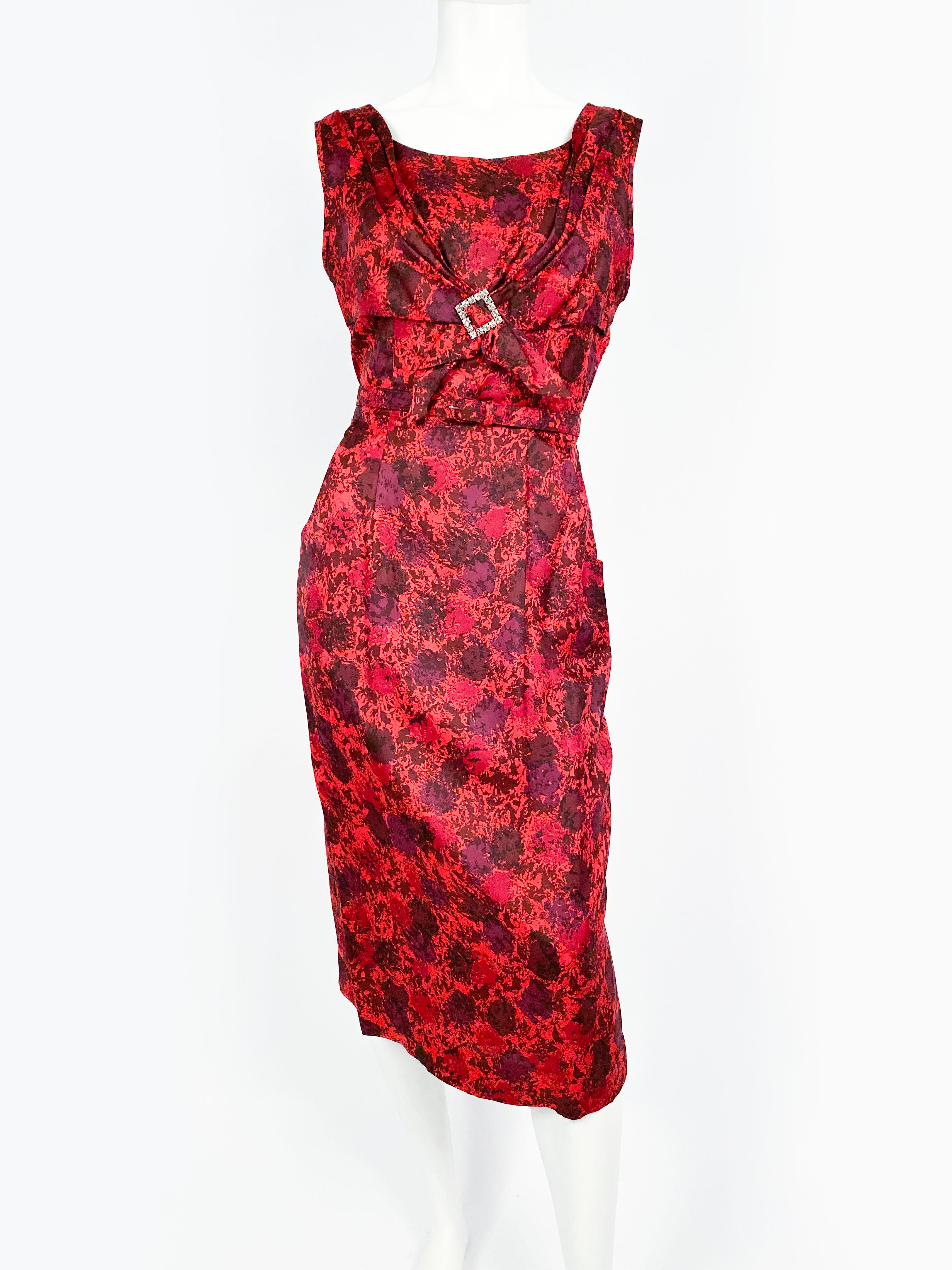 1950s red silk dress featuring a floral-like impressionist print with several tones of red. The bodice has a scoop neckline, an attached gathered panel that is finished with a rhinestone buckle. The skirt of the dress also has two front pocket.