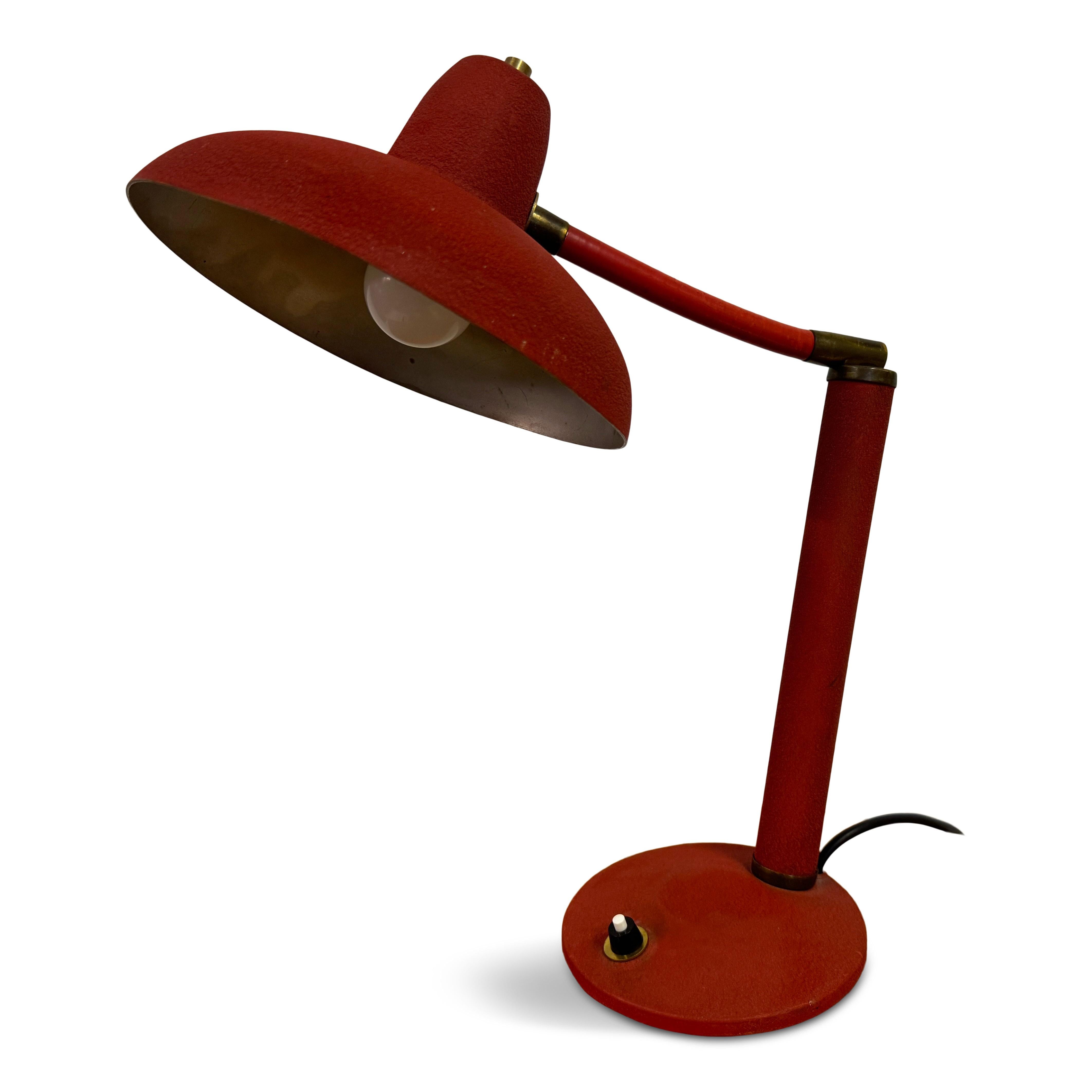  A vintage table lamp, from the 1950s, with a distinctly mid-century modern design. The lamp features a textured red finish that adds a vibrant and retro flair to its appearance. The shade is a wide, conical shape that directs light downwards, ideal
