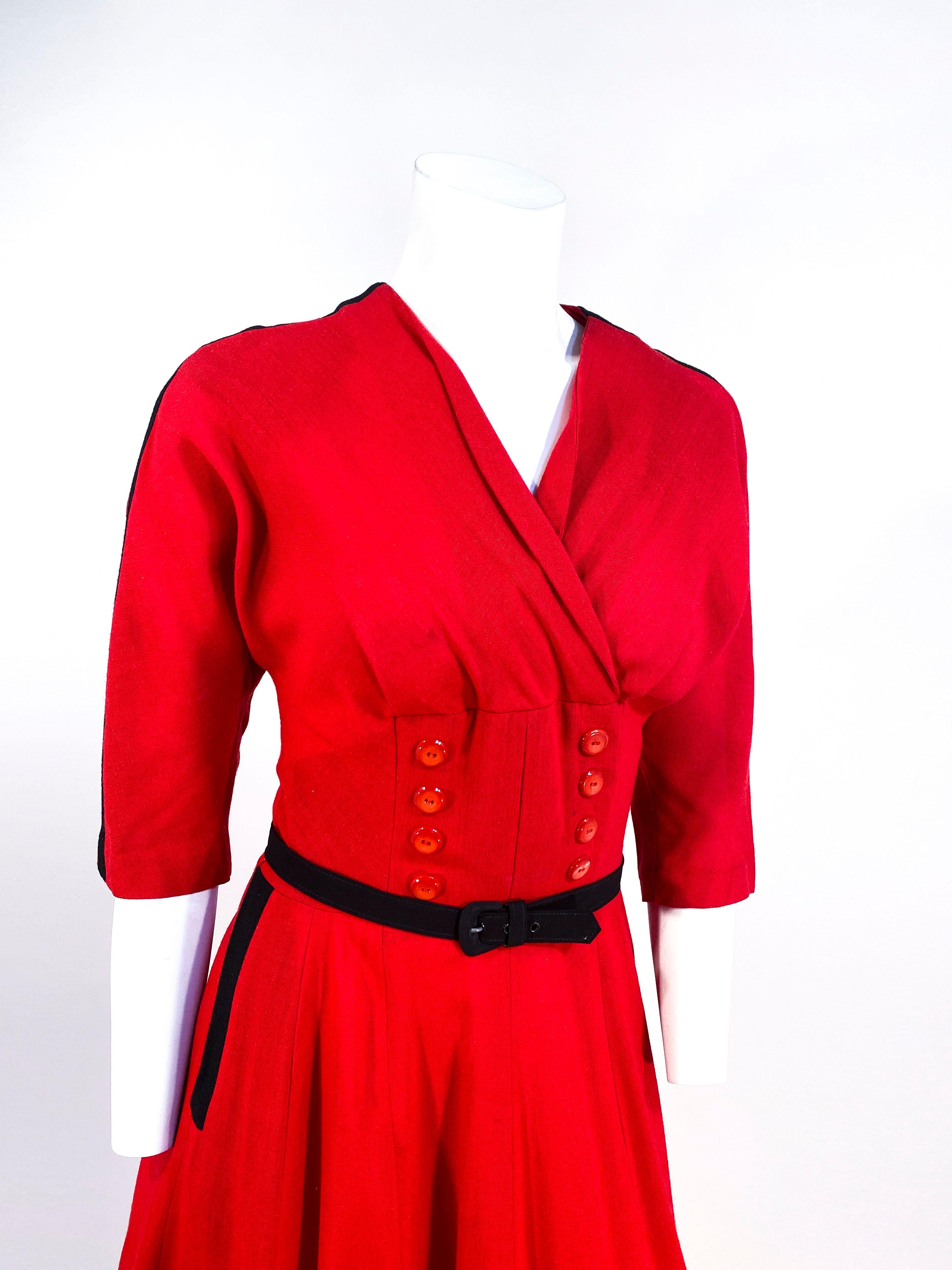 1950s red lightweight wool dress with full skirt, black bordered in-set side pockets, to match the black boarders on the three-fourths Dolman sleeves, and narrow black belt. The bodice is a gathered cross-over v-neck over a buttoned decorative