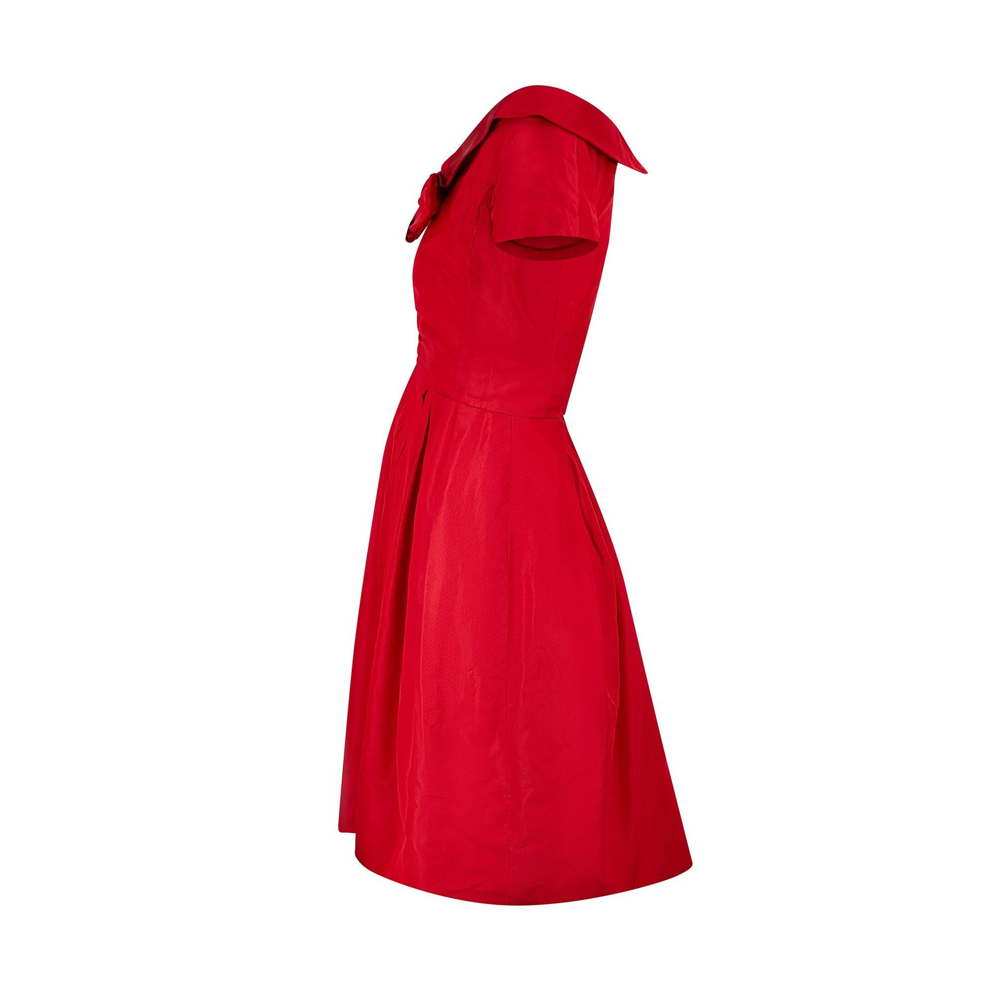 This colour-block red silk cocktail dress was manufactured in America in the mid-1950s. The off-the-shoulder tailoring adds a playfully sensuous detail, whilst the cap-sleeves, cinched waist and pleated full skirt are trademarks of the era. The