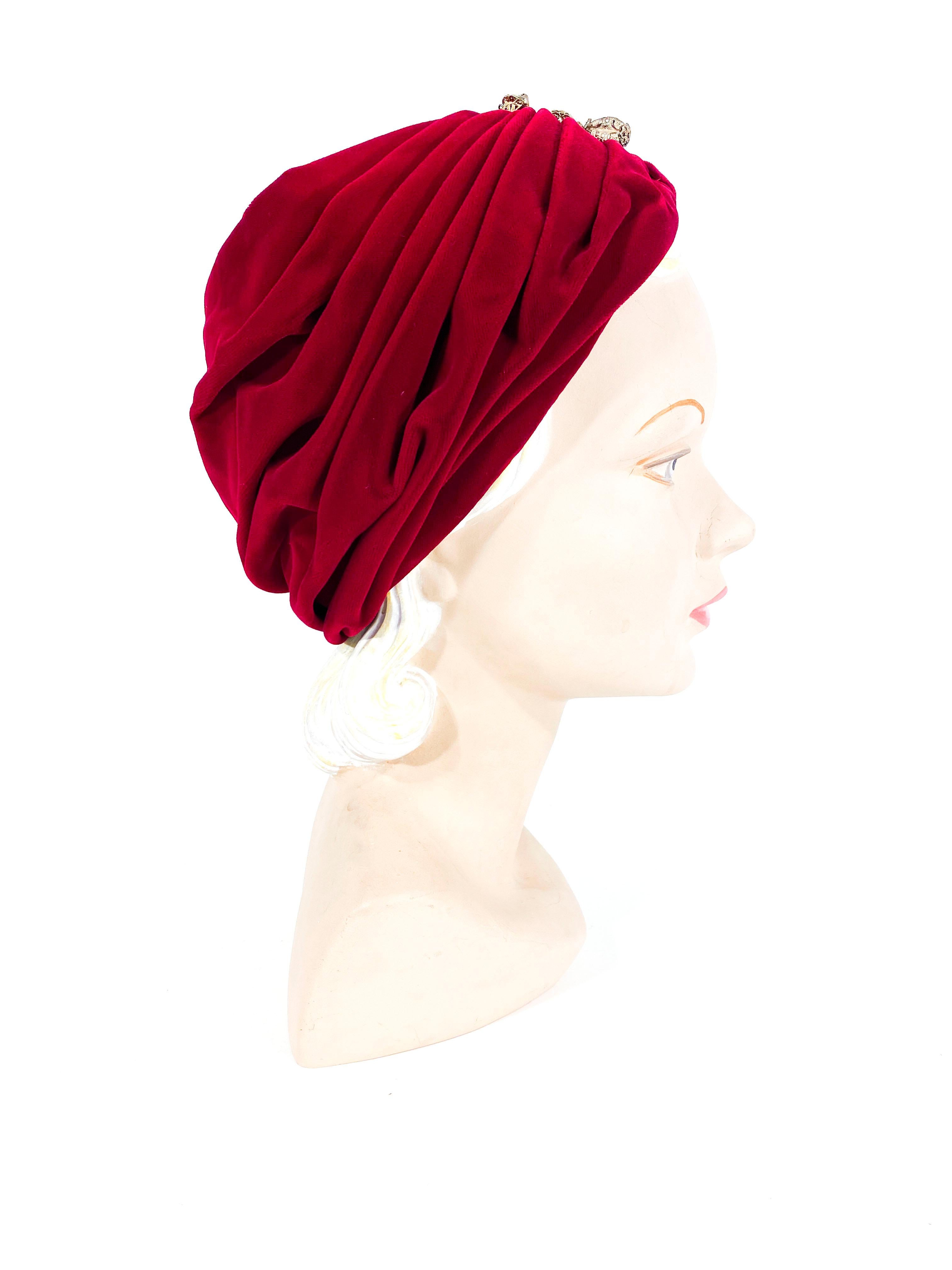 1950s red rayon velvet hand ruched turban decorated with a hand pierced brass and faux tiger's eye ornament. The interior is lined in net finished with a grosgrain ribbon. 