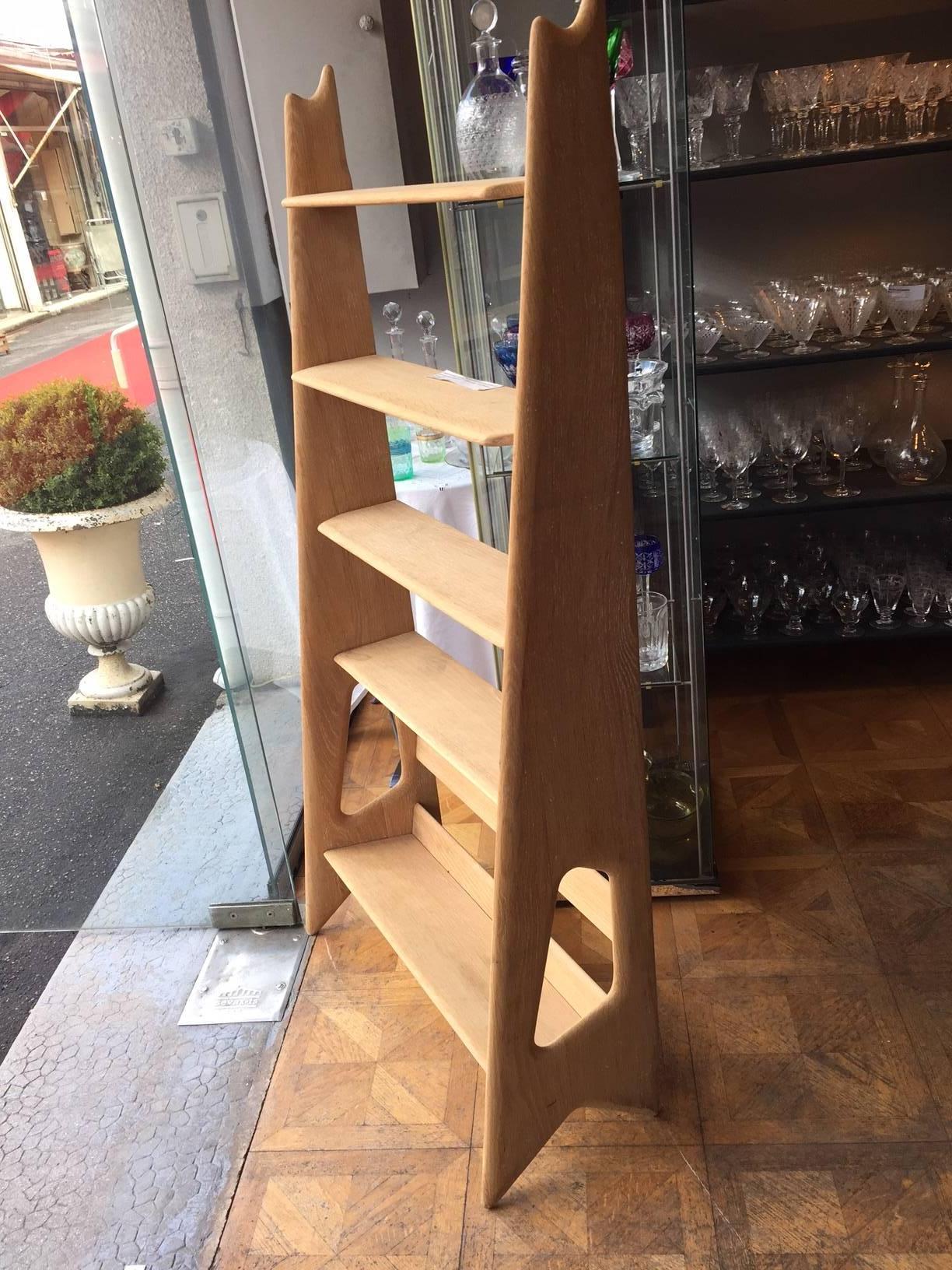 Designed with an organic design, has five shelves with different depths.
Made of solid oak with a natural finish.
The uprights go straight up at the back and at the front they go up in the form of a point.
On the lower part an opening in the wood