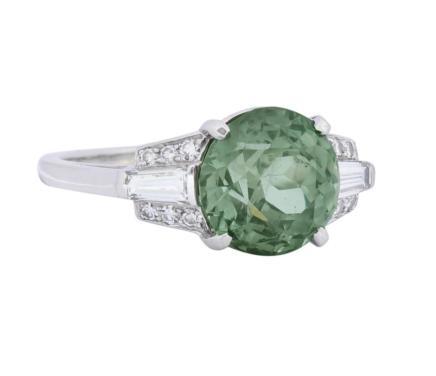 Basket cathedral style ring centering a round cut alexandrite weighing 5.05 carats, transparent and a striking yellowish-green in daylight

Alexandrite color changes to a light grayish-purple when exposed to incandescent light

Flanked by two bar