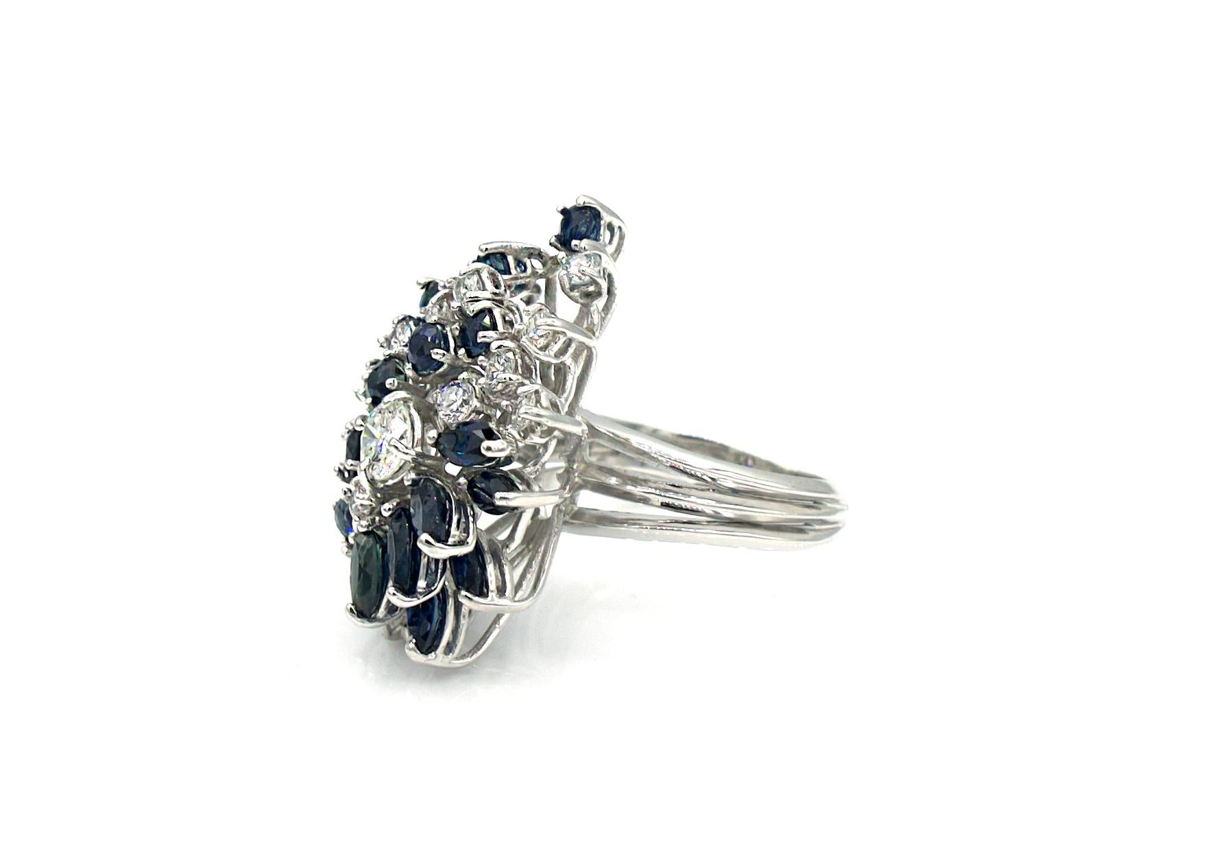 This 1950s Retro ring is made of a combination of shiny marquise-cut and round-cut blue sapphires and diamonds that coalesce in layers and cluster around a slightly larger center diamond, weighing 3 Carats total. The sapphires and diamonds are