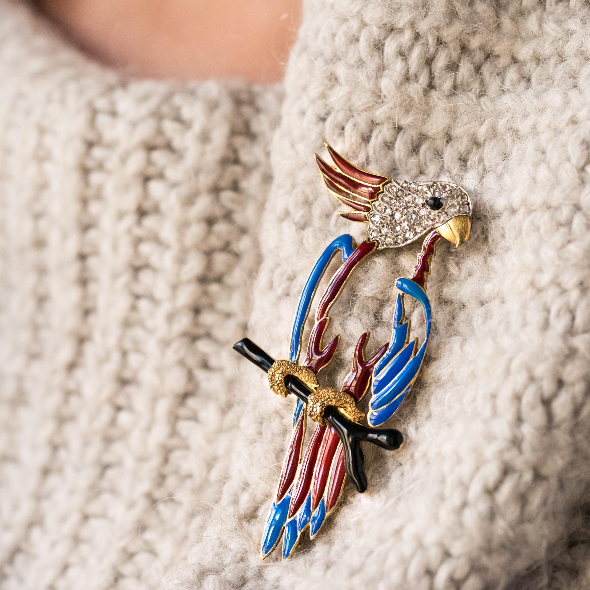 Brooch in 18 karats yellow gold, owl hallmark.
This incredible retro brooch represents a parrot whose body is pierced and enamelled blue and red. The bird is resting on a black enamelled gold branch. His head is set with rose-cut diamonds and red