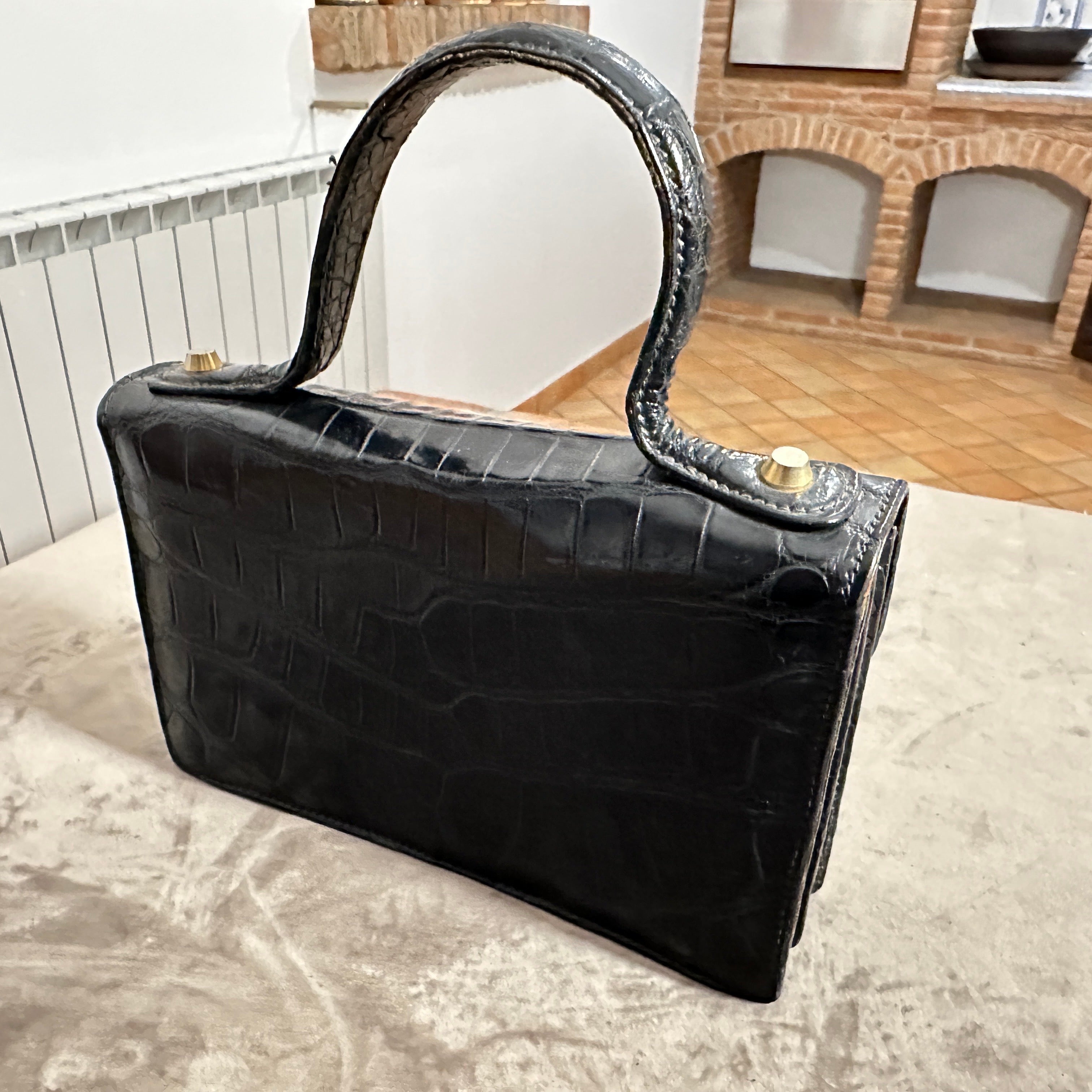 Entrez dans une ère de glamour raffiné avec cet exquis sac à main du soir des années 1950, où le cuir de veau gaufré en croc d'un noir profond occupe le devant de la scène et où le poids réconfortant de la quincaillerie en laiton massif souligne sa