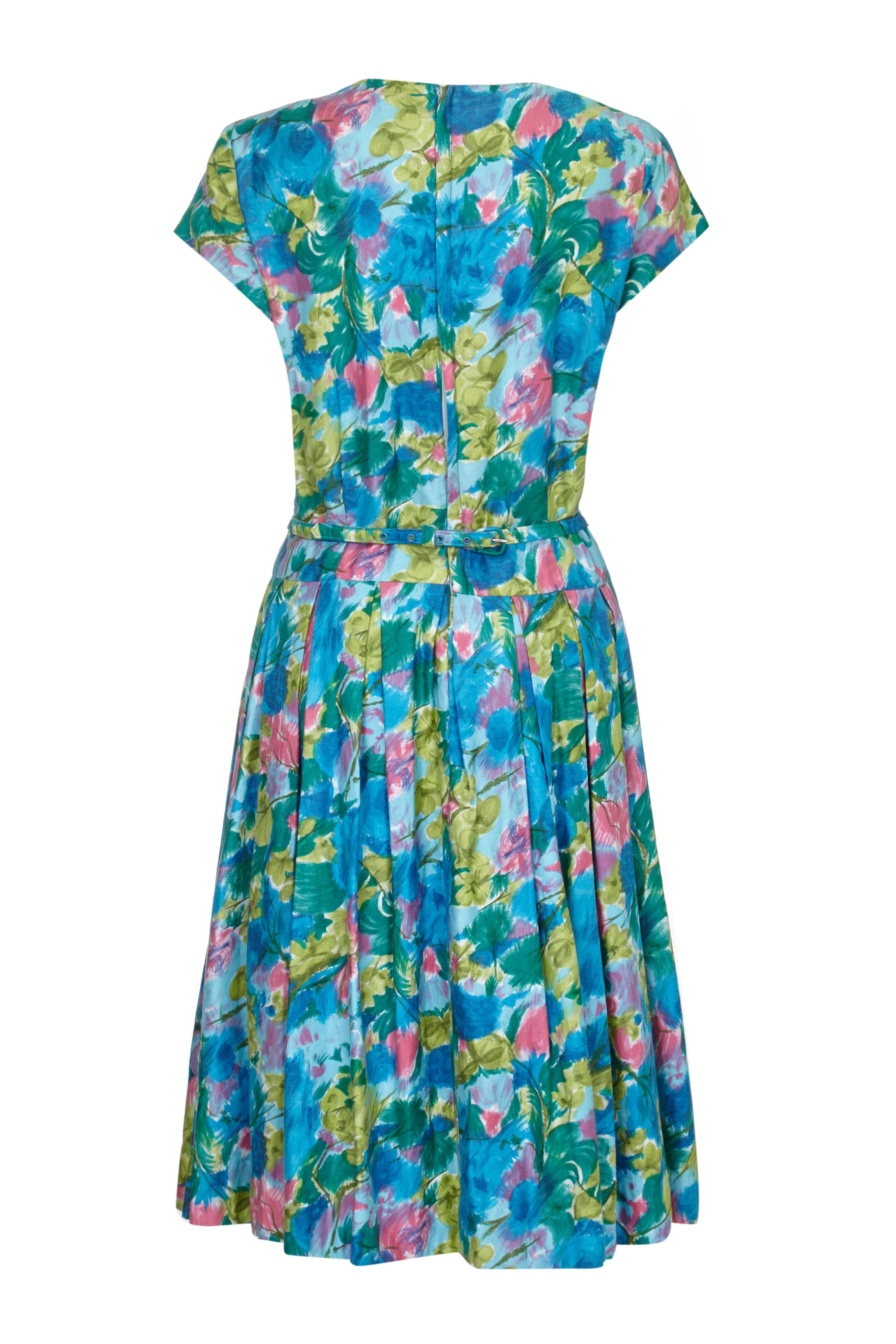 This lovely Riddella 1950s or early 1960s cotton dress with abstract floral print in green blue and pink is vivacious, versatile and a great choice for the Summer. It features princess seams on the bodice with green piping and bow details at the