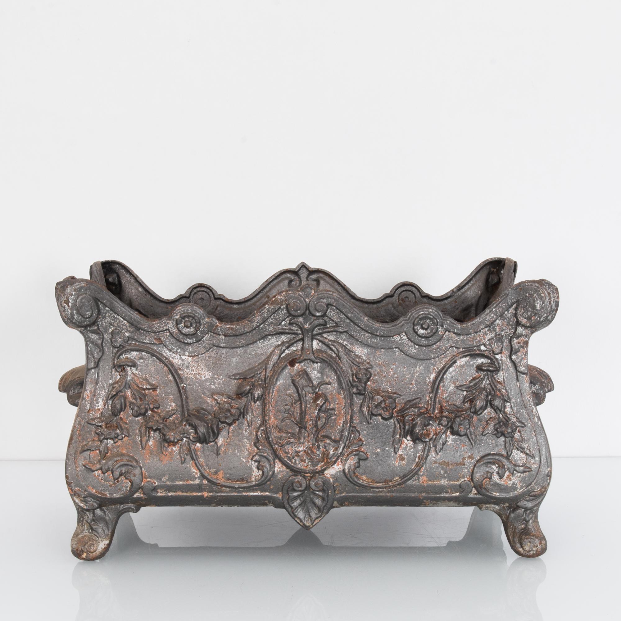 A vintage cast iron planter from 1950s France, with a distinctly Rococo silhouette. A gently serpentine trough with scrolled and scalloped edges sits upon raised feet, and features elaborate embellishment; flowers, leaves, shells and rosettes. A