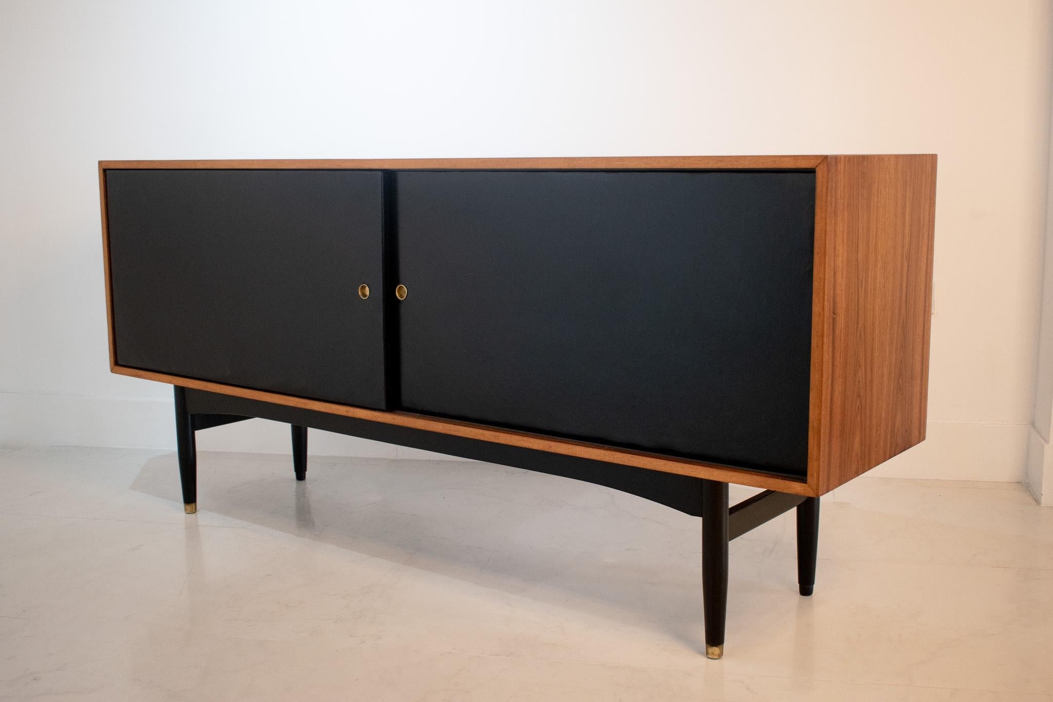 A stunning and extremely rare sideboard / credenza designed by the British designer Robin Day and manufactured by Hille, 1950s. 

This piece consists of a rosewood body, ebonized wooden legs with brass feet with black leather sliding doors.
