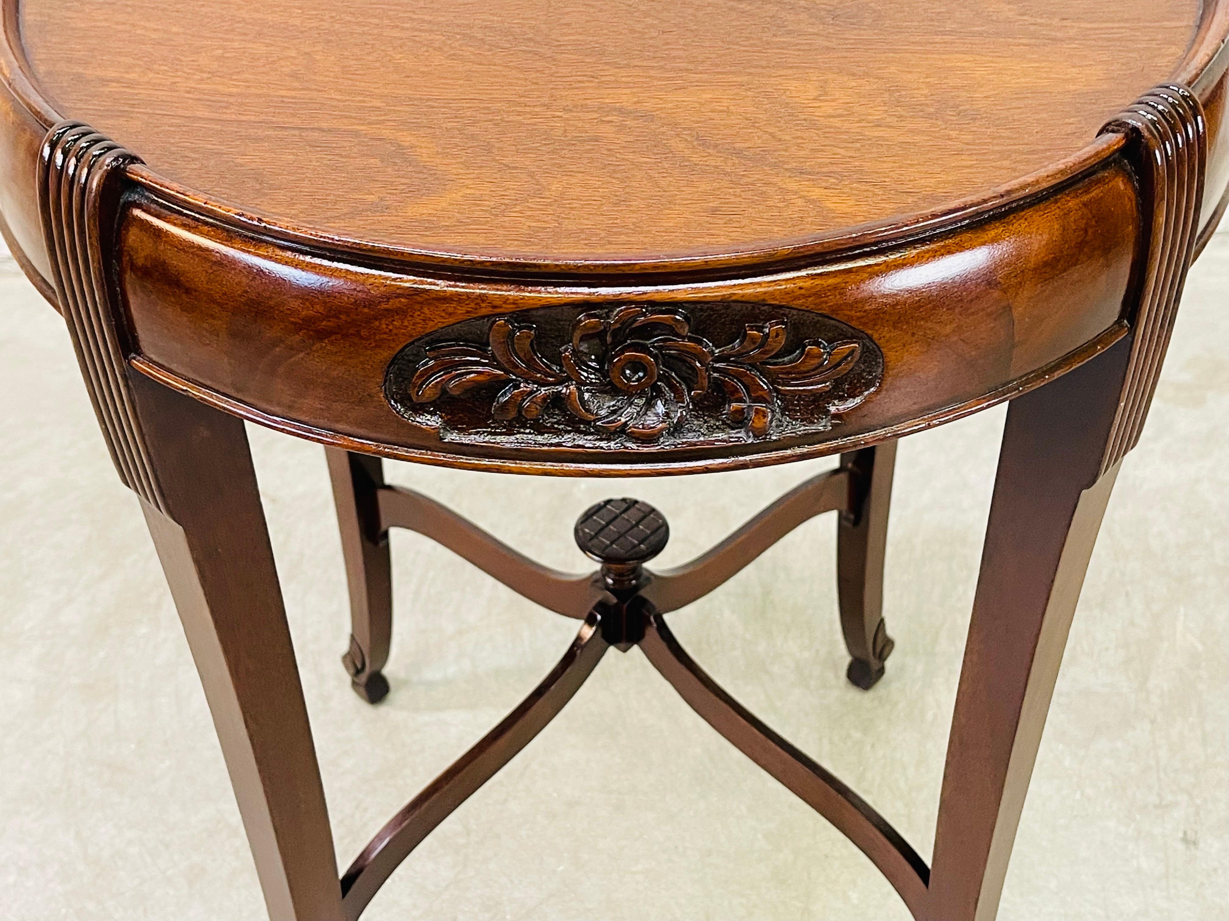 Vintage 1950s round mahogany floral carved side table. The table has carved accents on top and on the feet. There is ornate carved supports in the middle. Newly refinished condition. No marks.