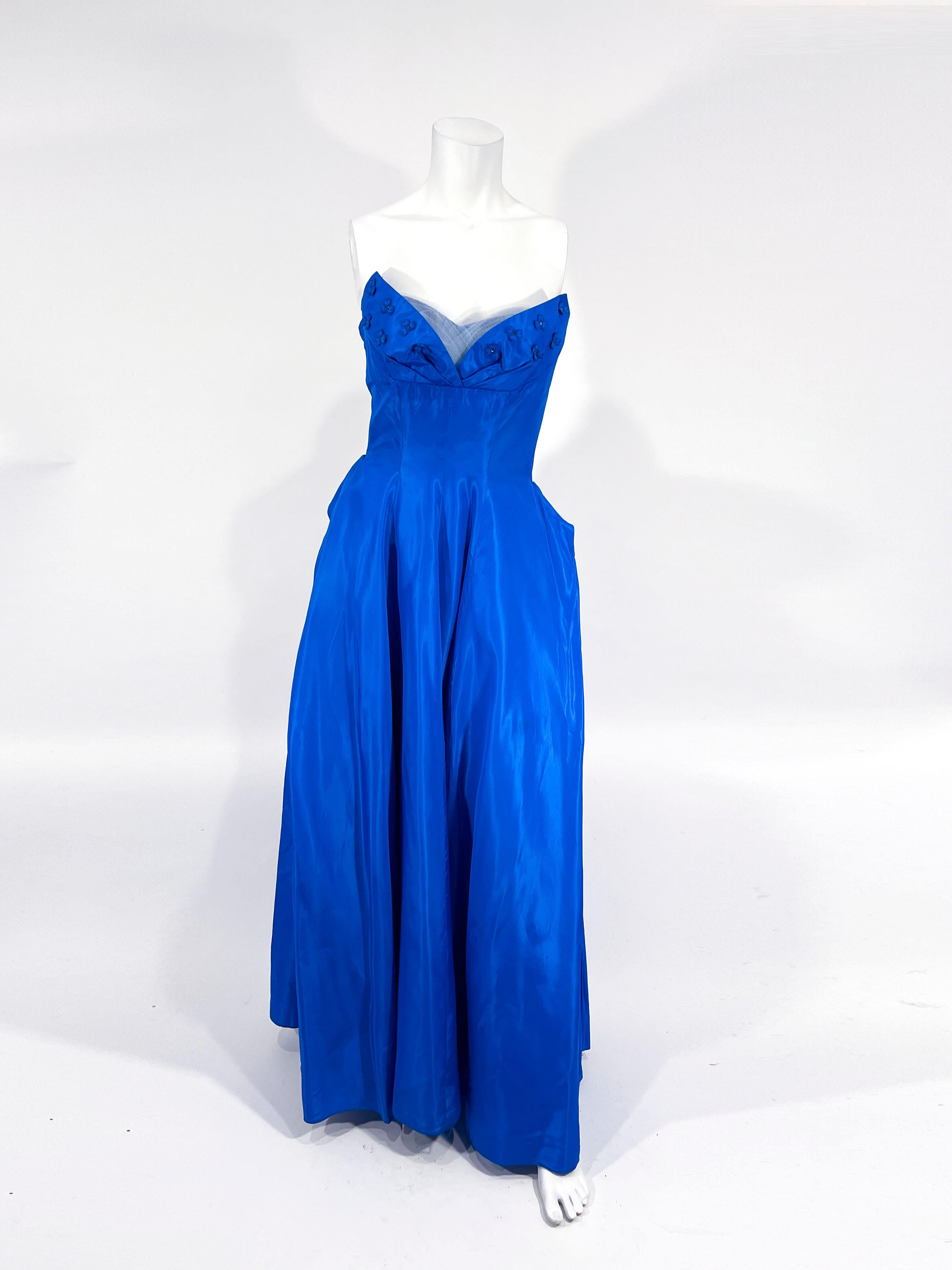 Königsblaues Taft-Ballkleid aus den 1950er Jahren mit herzförmigem Ausschnitt, überlagert von einer plissierten Tüllverkleidung und verziert mit Strassblumen-Applikationen. Der bodenlange Rock ist im Rücken stark gerafft und mit einer eingenähten