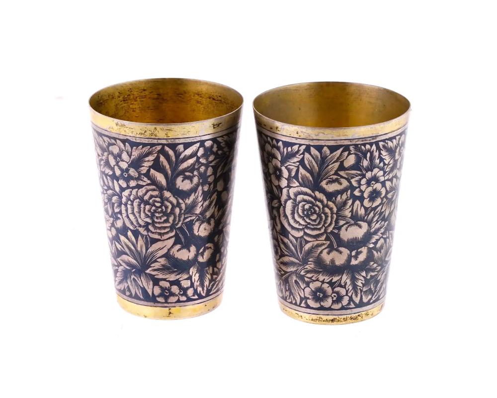 A pair of Russian Soviet era silver cups. Made in Veliky Ustyug, Northeast Russia. The bodies are decorated with a niello flowers and berries pattern. The rims and the interior are gilt. Both items have a 875 silver standard mark and SCh7 assay mark
