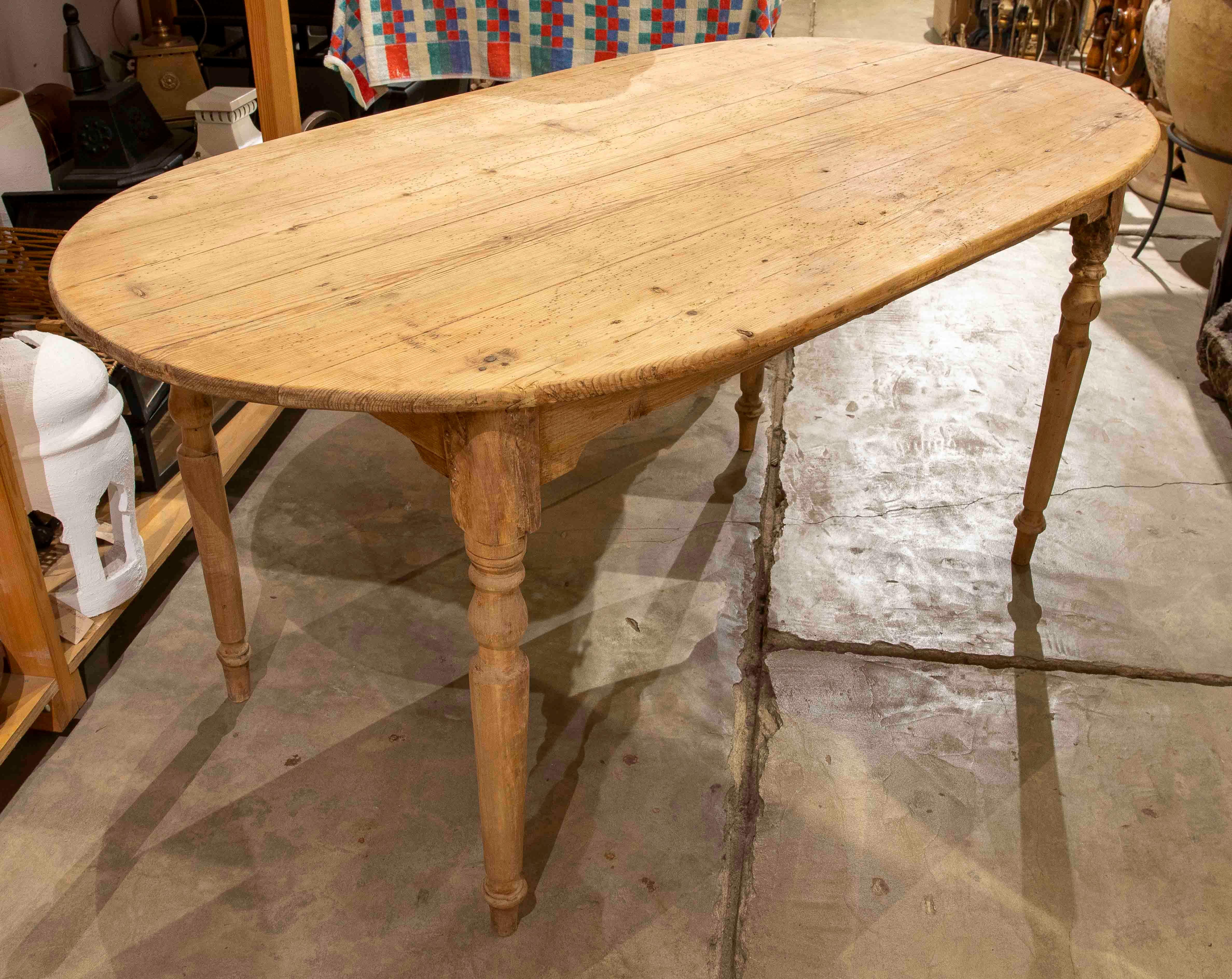 Cette belle table rustique présente une forme ovale et est fabriquée en bois de pin naturel, montrant une finition vieillie qui met en valeur l'authenticité de son design. Ses pieds tournés ajoutent un détail classique et élégant qui s'associe