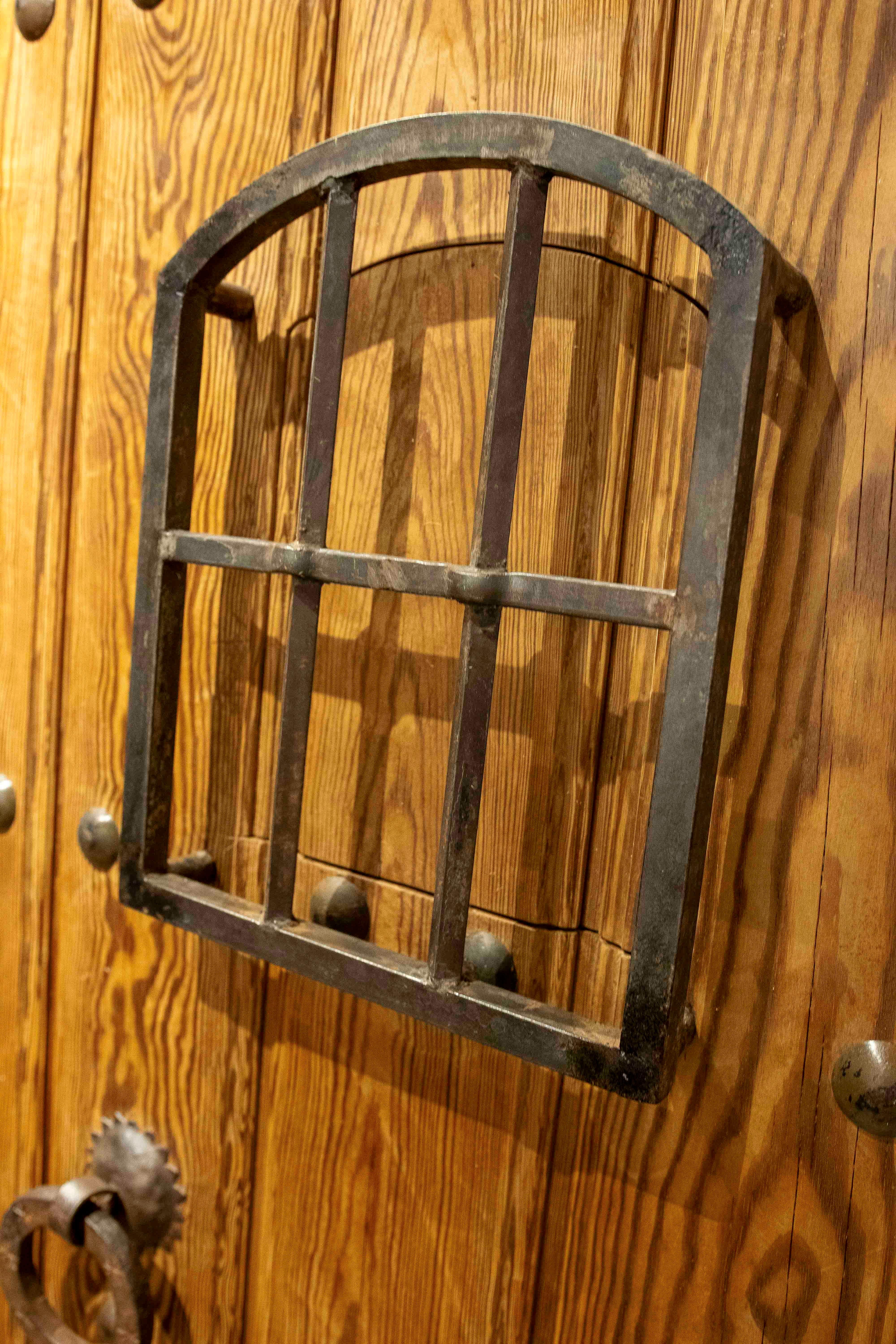 Magnifiche porte doppie spagnole realizzate in legno massiccio, con un design rustico che riflette le tradizioni artigianali della penisola iberica. Ogni anta è rinforzata da grandi chiodi decorativi in ferro battuto che aggiungono robustezza e