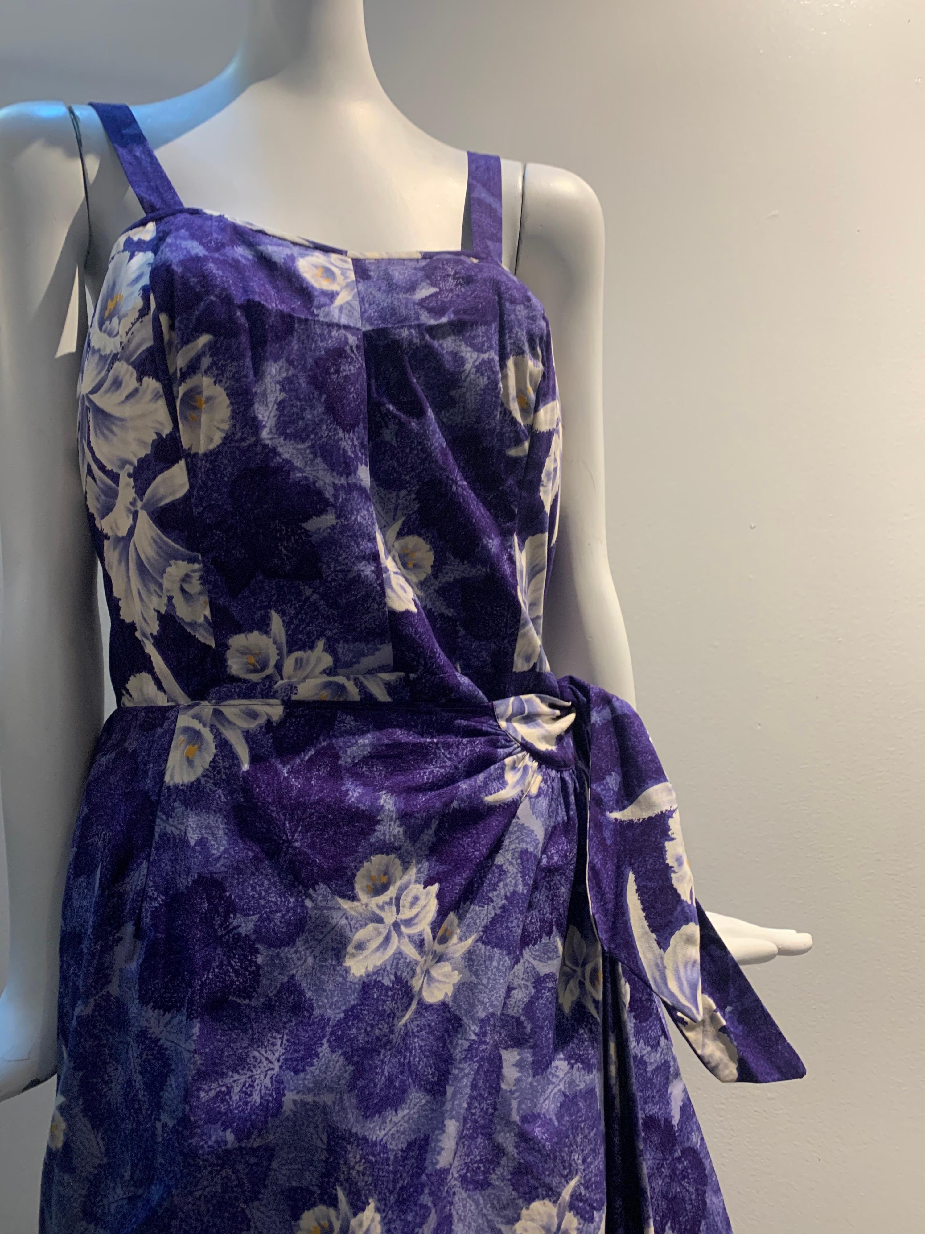 robe de soleil en coton de style sarong des années 1950, avec un imprimé tropical violet et des orchidées blanches éparpillées. Fermeture à glissière au dos, panneaux latéraux élastiques, jupe enveloppante avec lien latéral. Le style classique de