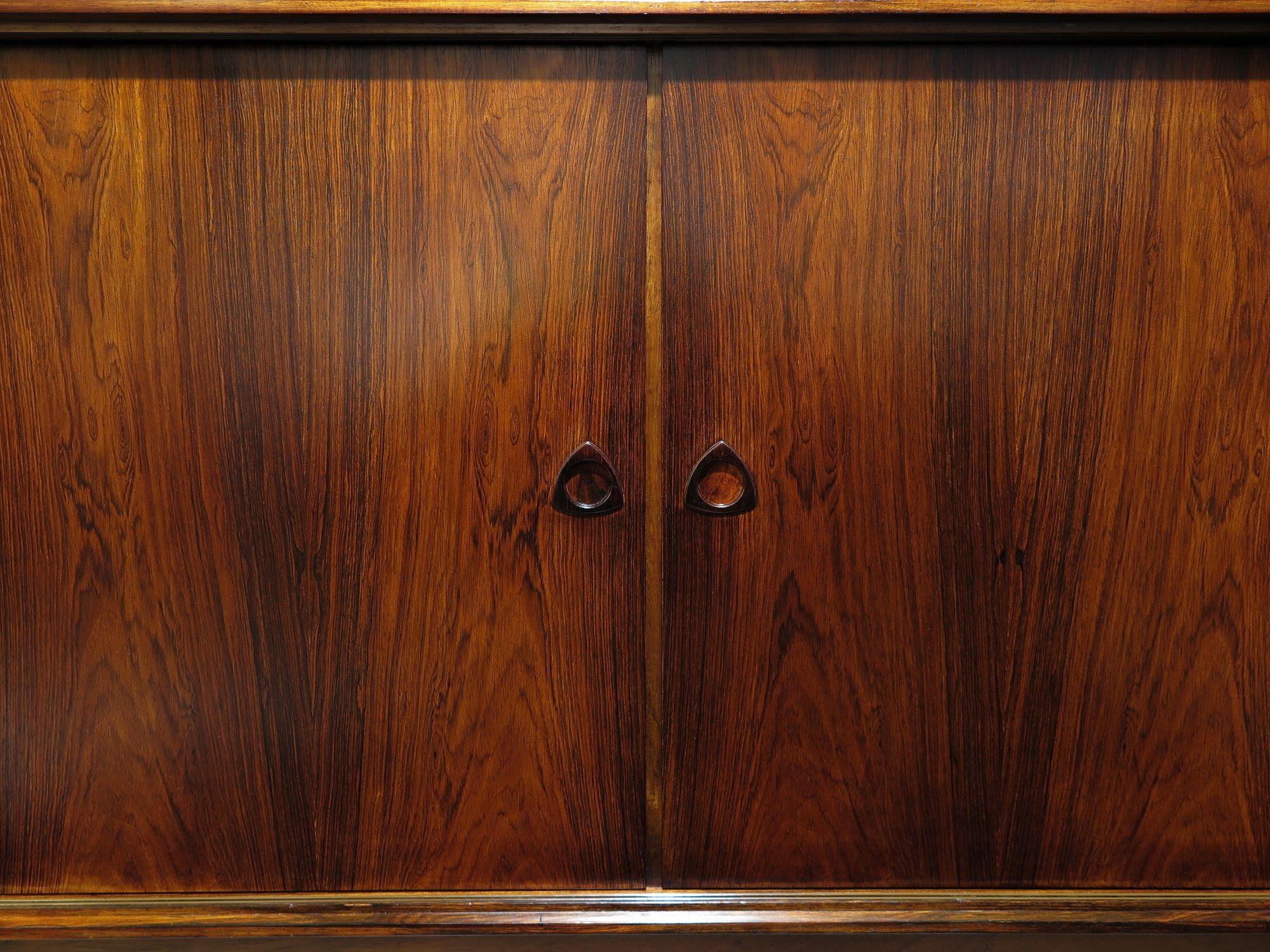 Este aparador danés artesanal de la década de 1950 es de palisandro oscuro de Brasil, con impresionantes veteados. Las puertas correderas se abren para revelar una barra central con una luz interior -que se activa automáticamente al abrir la puerta-