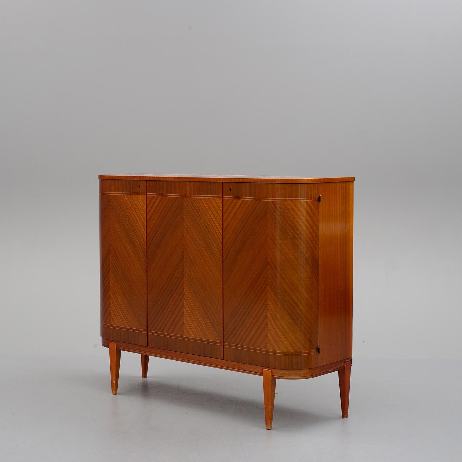 A three-door mahogany sideboard, the veneer forming a superb chevron pattern, internally fitted with adjustable shelves and drawers, with curved doors and sides, on tapered legs, with brass bullet hinges, brass locks and original key in working