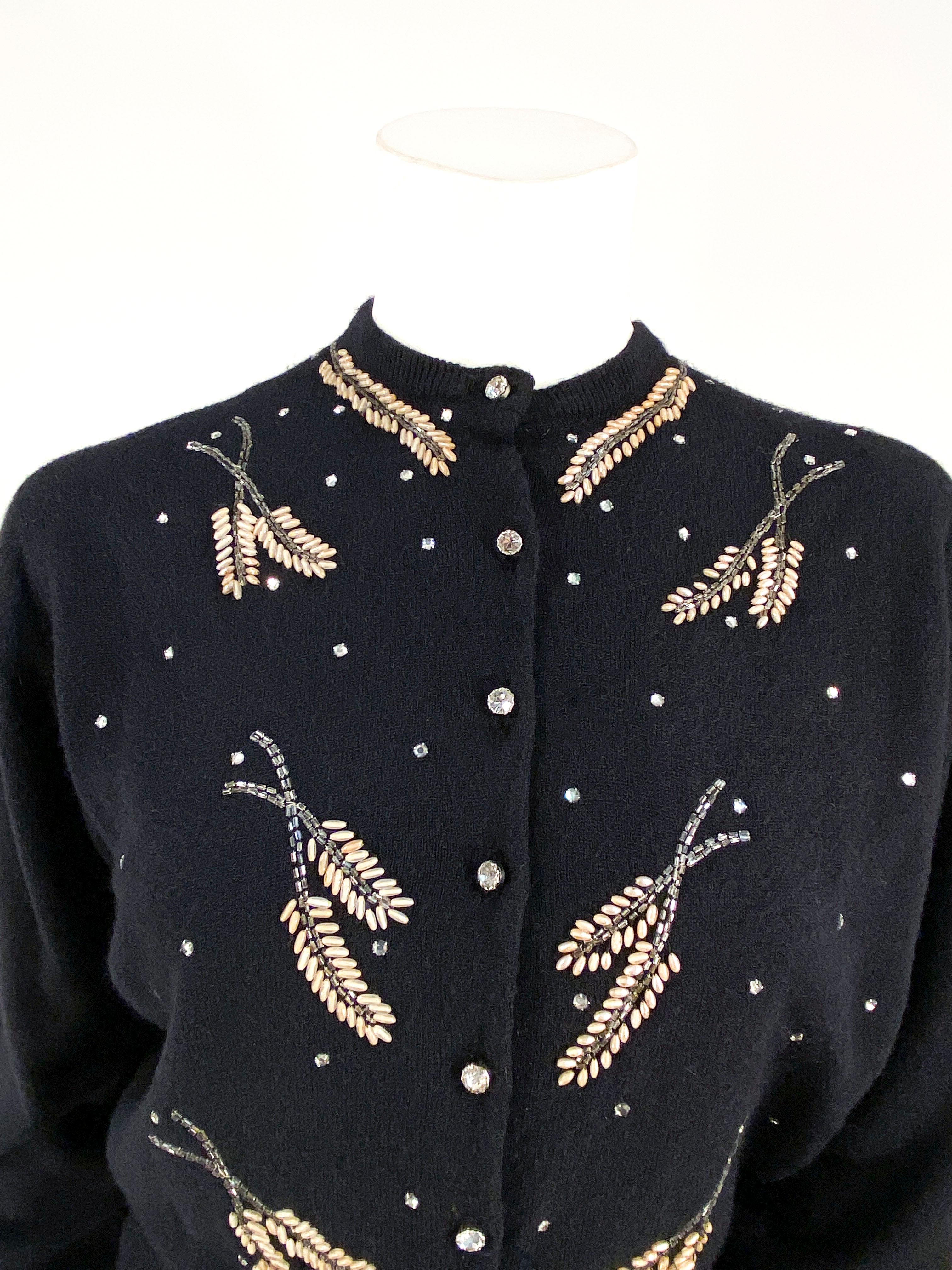 1950s Schiaparelli black cashmere cardigan sweater with large rhinestone studding and beadwork set in leaf patterns. The front has large rhinestone buttons on the front closure, the cuff ribbing is elongated to be worn in a rolled-up cuff fashion