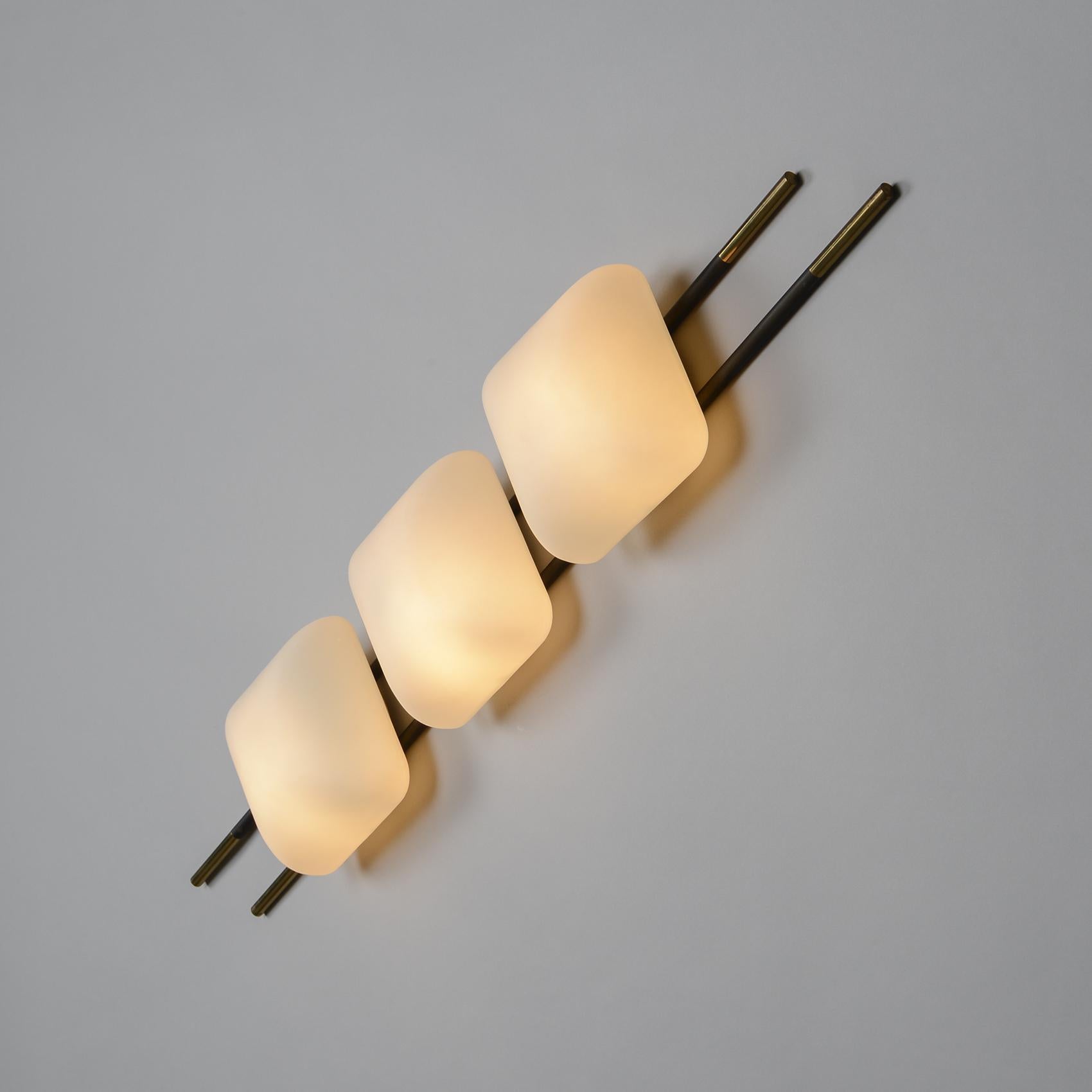 Large three-light wall sconce, dating back to the 1950s and created by the french manufacturer Maison Lunel.

We like the elegance of the structure, composed of wooden and brass rods, which holds three opaline glass reflectors, diffusing a soft