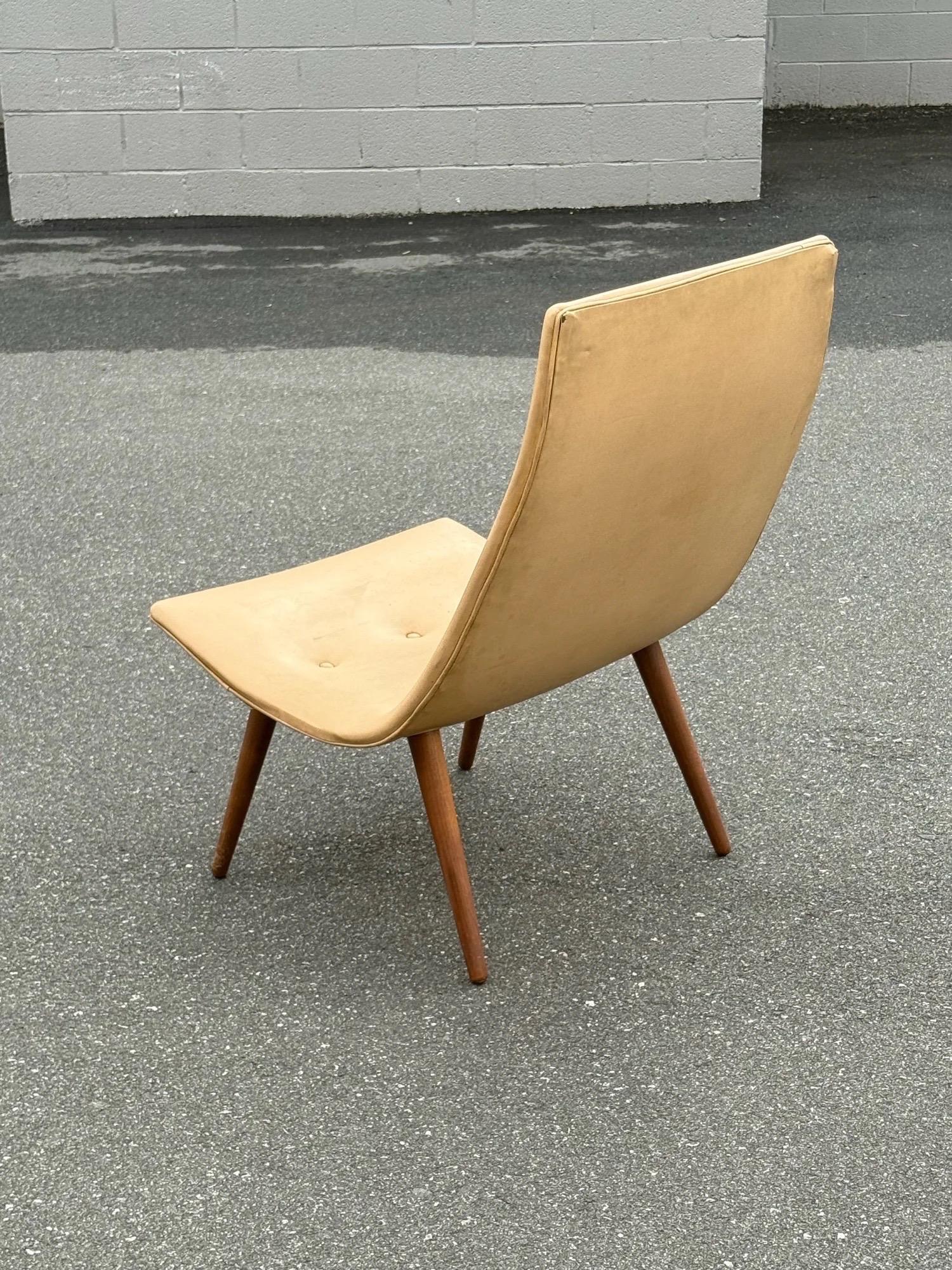 Salón de una sola pala de los años 50 atribuido a Allan Gould. El respaldo alto que se introduce en el asiento crea un perfil único. Un diseño minimalista asentado sobre cuatro patas de madera cónicas y acampanadas. Esta pieza presenta la tapicería