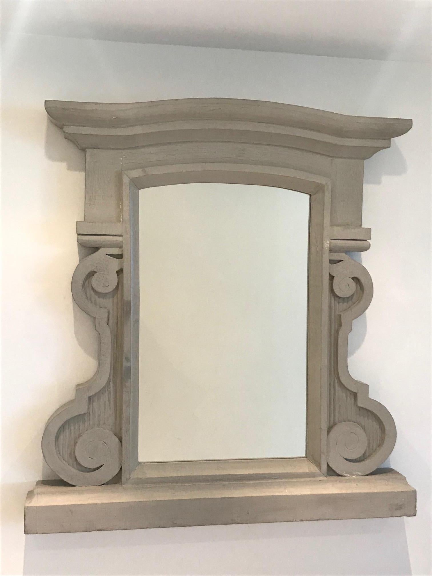 Vintage French mirror comprised of solid and heavyweight reclaimed wood. Mirror features a gorgeous hand carved frame with large chiseled scrolls and fluted details. Has curved pediment top and thick stepped shelf base. Painted in grey / beige by