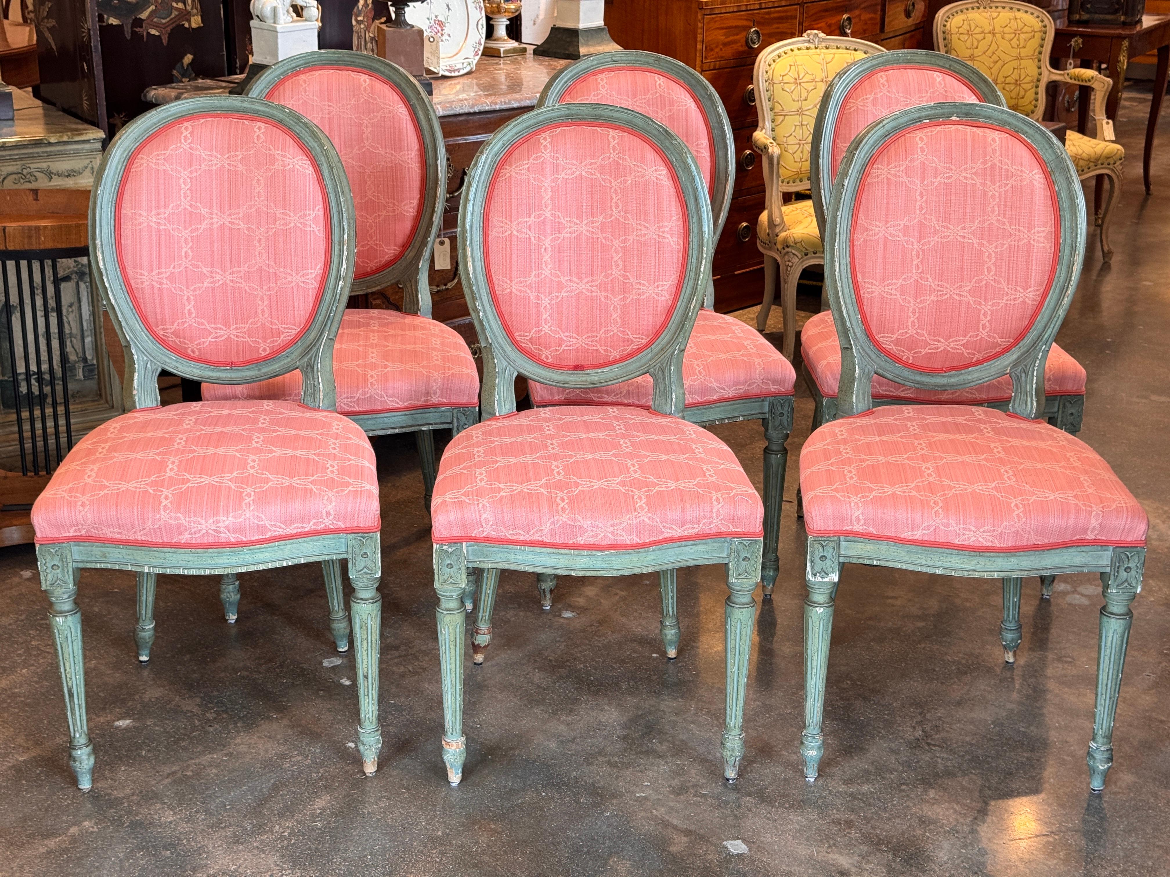 Satz von sechs Esszimmerstühlen im Louis XVI-Stil mit geschnitzten ovalen Rückenlehnen und kannelierten Beinen mit Rosetten-Details. Die lackierten Rahmen weisen ein abgenutztes grünes Finish mit leichten Gebrauchsspuren auf, gepaart mit