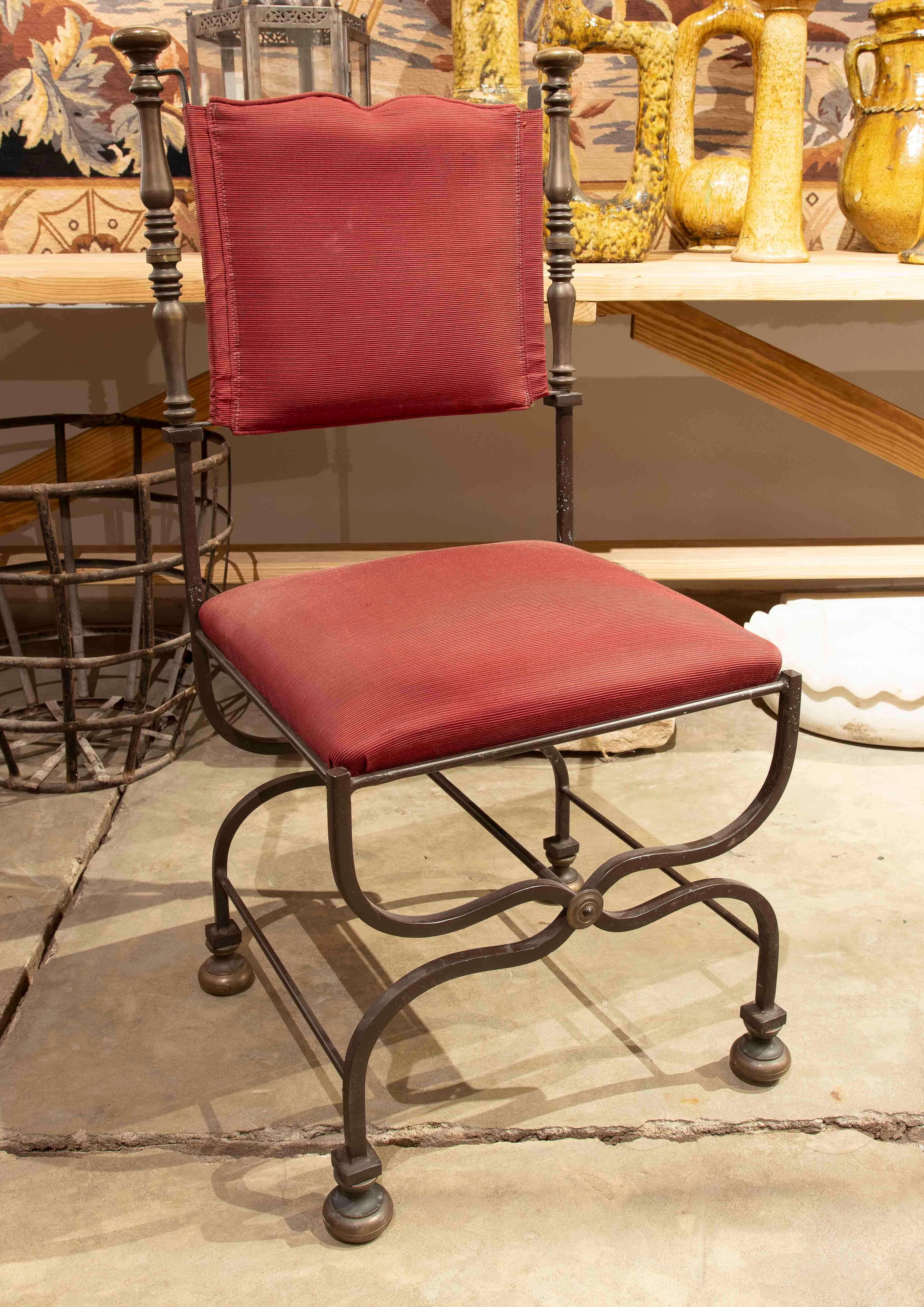 Elegant set of eight wrought iron chairs with a classic and refined design. The metal frame features turned details and a base with curved crossbars for stability and style. The seat and backrest are upholstered in a warm red tone, providing comfort