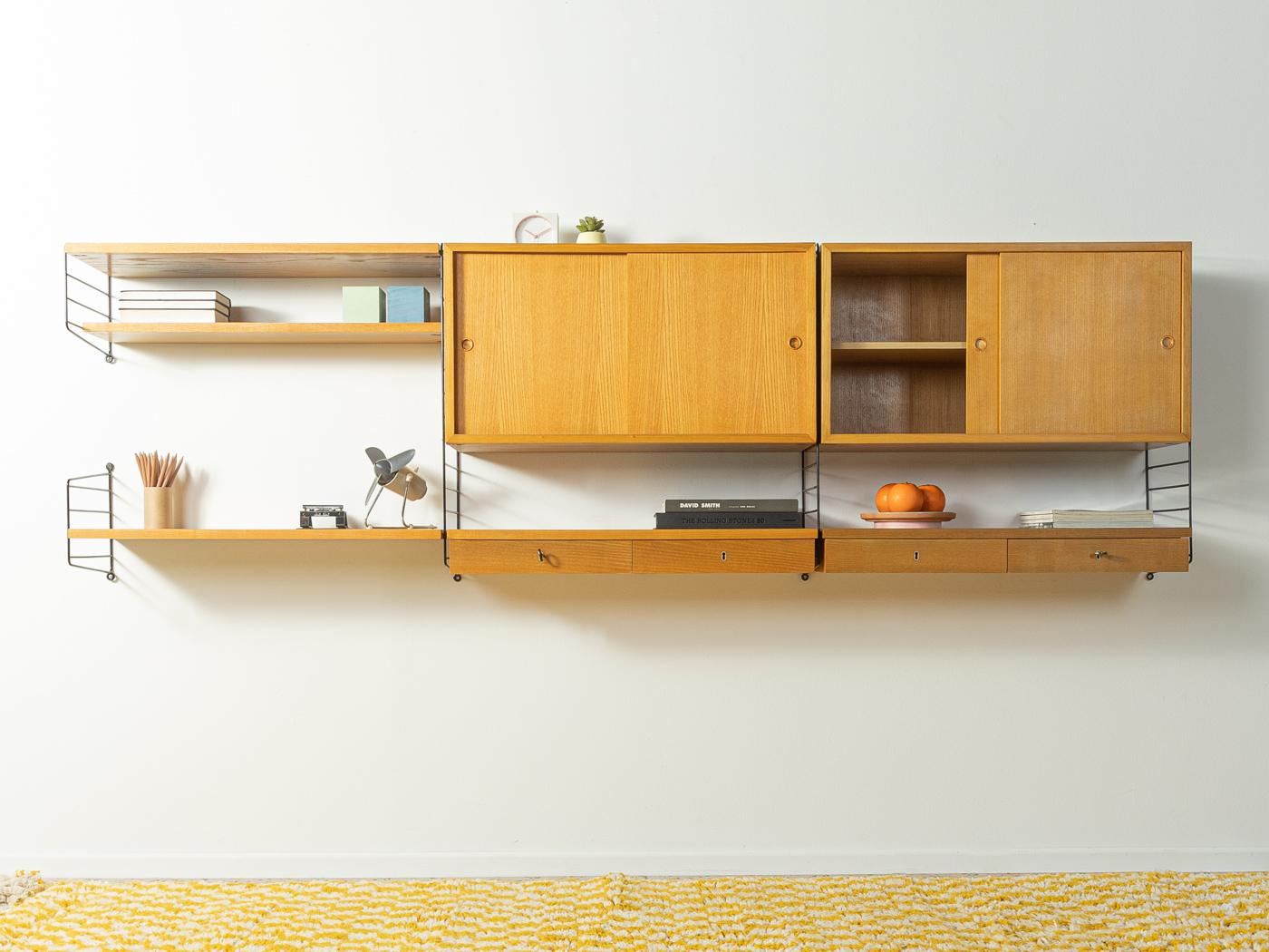 Original String shelf designed in 1949 by Nils Strinning in ash veneer. The system consists of five metal ladders in white with three shelves, two containers with sliding doors and two containers with drawers.

This original String shelf is much