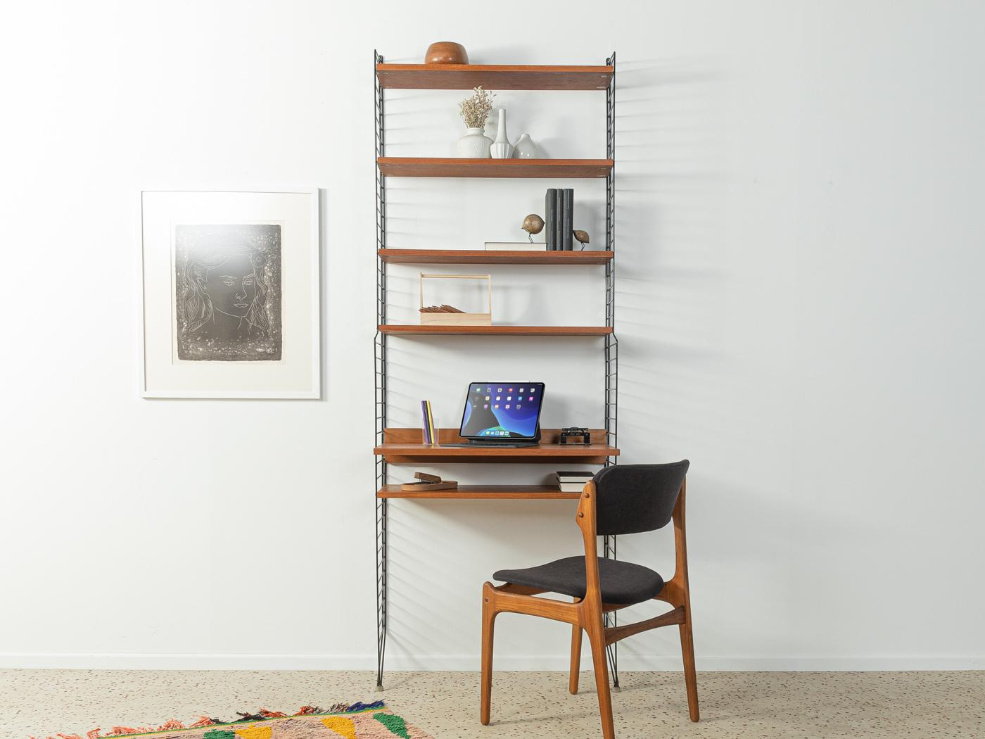 Original String shelf designed in 1949 by Nils Strinning in teak veneer. The system consists of two metal ladders in black with four small shelves, one large shelve and a bureau compartment.

This original String shelf is much better processed and