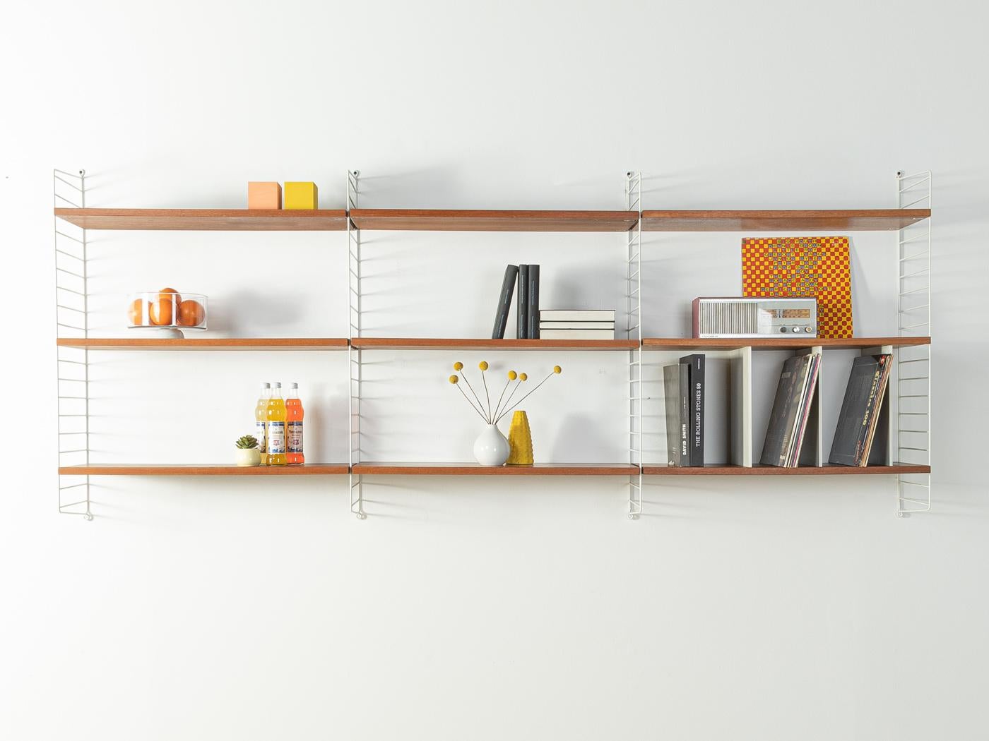 Original String shelf designed in 1949 by Nils Strinning in teak veneer. The system consists of four metal ladders in white with nine shelves and three rare white lacquered vinyl dividers.

This original String shelf is much better processed and