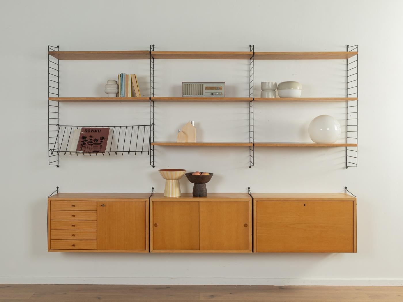 Original String Shelf designed in 1949 by Nils Strinning in ash veneer. The system consists of eight metal ladders in black with eight shelves, a magazine rack, one container with five drawers and a door, one container with sliding doors, a