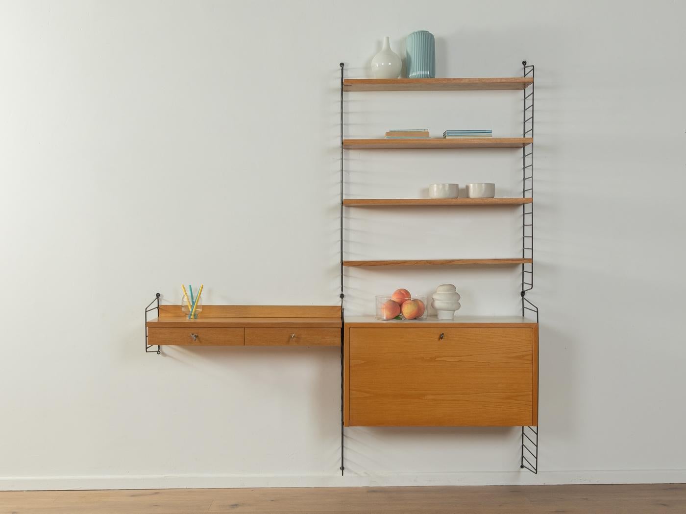 Original String shelf designed in 1949 by Nils Strinning in ash veneer. The system consists of five metal ladders in black with four shelves, one container with two drawers and one container with hinged door and different storage compartments. The