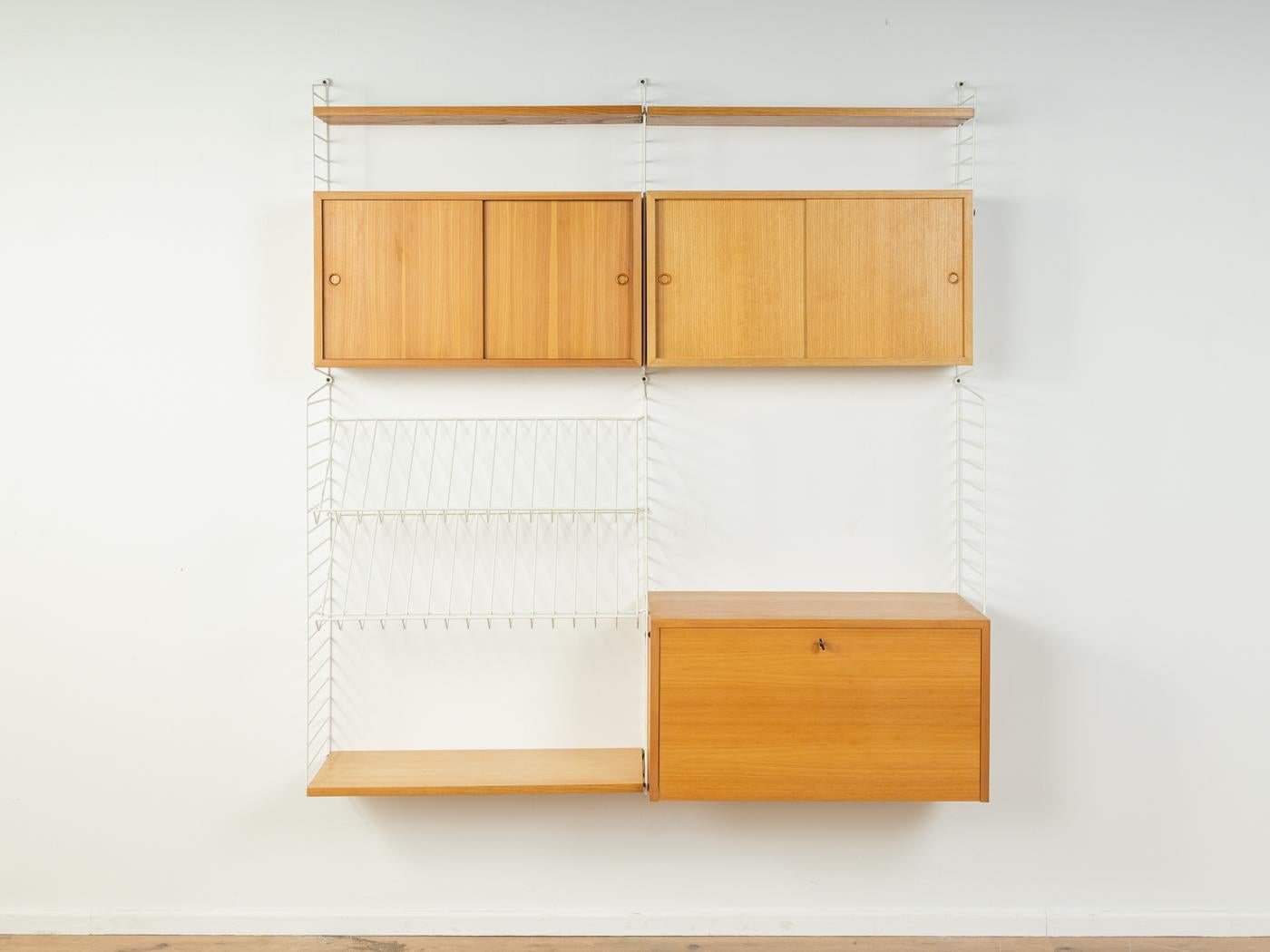 Original String shelf designed in 1949 by Nils Strinning in ash veneer. The system consists of six metal ladders in white with three shelves, two containers with sliding doors, one container with a flap door with many compartments and three internal