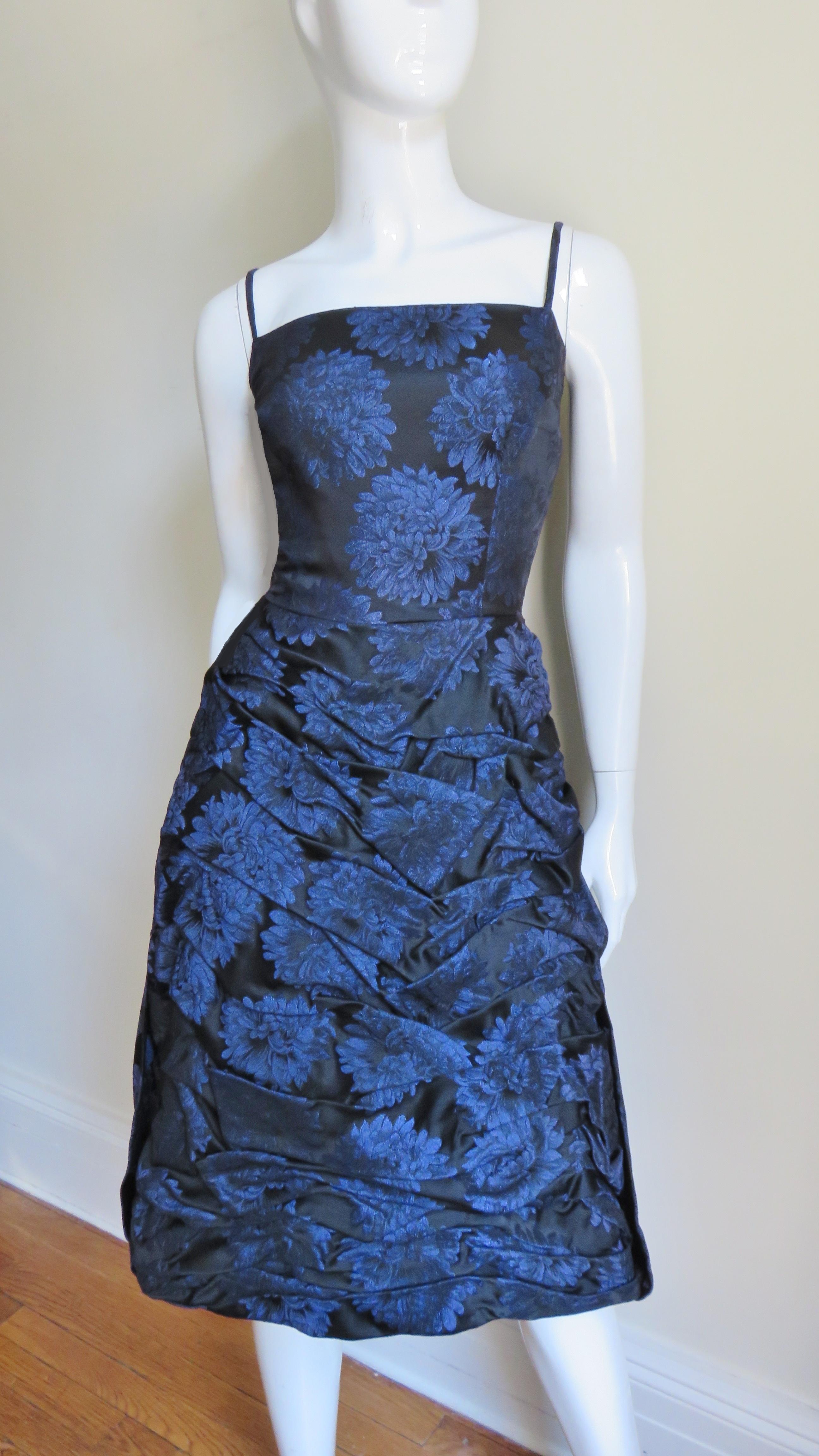 A fabulous blue on black chrysanthemum pattern silk damask dress by Sher Lee.  It has a fitted bodice with spaghetti straps and an incredible ruched skirt.  The back has a waterfall drape from the waist to skirt hem.  It is fully lined in black silk