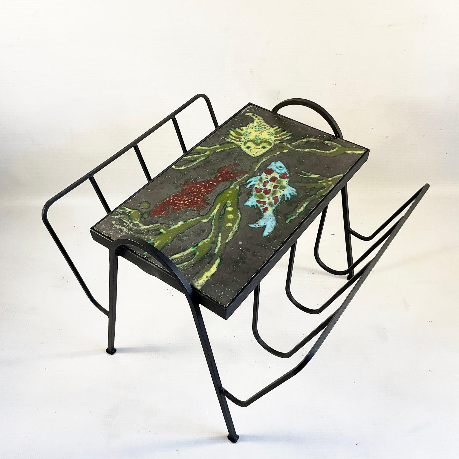 Rare 1950s wrought iron and lava enamel side table with magazine rack attributed to Guidette Carbonell and Jacques Adnet.
A wrought iron base with one enamel plaque created a marine decoration.