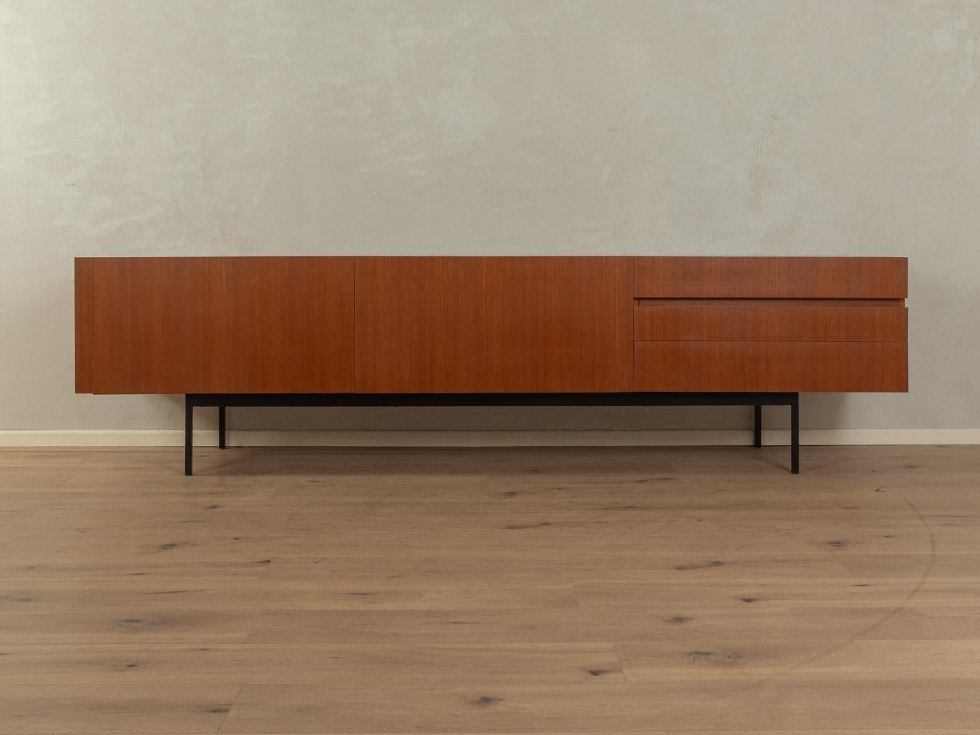 Puristic sideboard from the 1950s by Dieter Wäckerlin for Behr Möbel, model B41. Corpus in teak veneer with three drawers, two folding doors, a bottle carrier, two shelves and squared steel feet in black.

Quality Features:

    accomplished design: