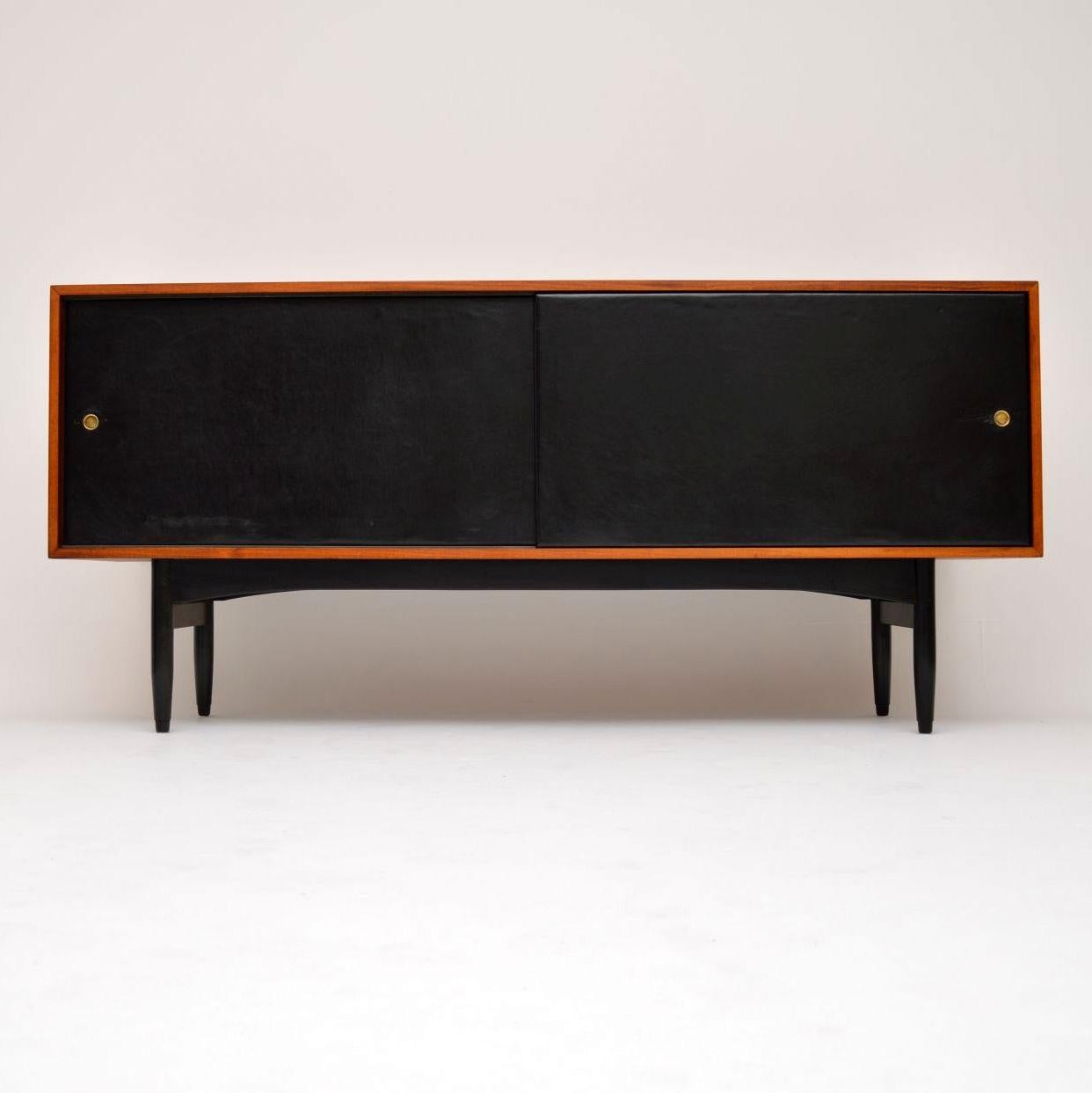 A stunning and extremely rare sideboard designed by the famous British designer Robin Day for Hille, this dates from the 1950s. It has ebonised wooden legs and black leather bound sliding doors. We have had the wood stripped and re-polished to a