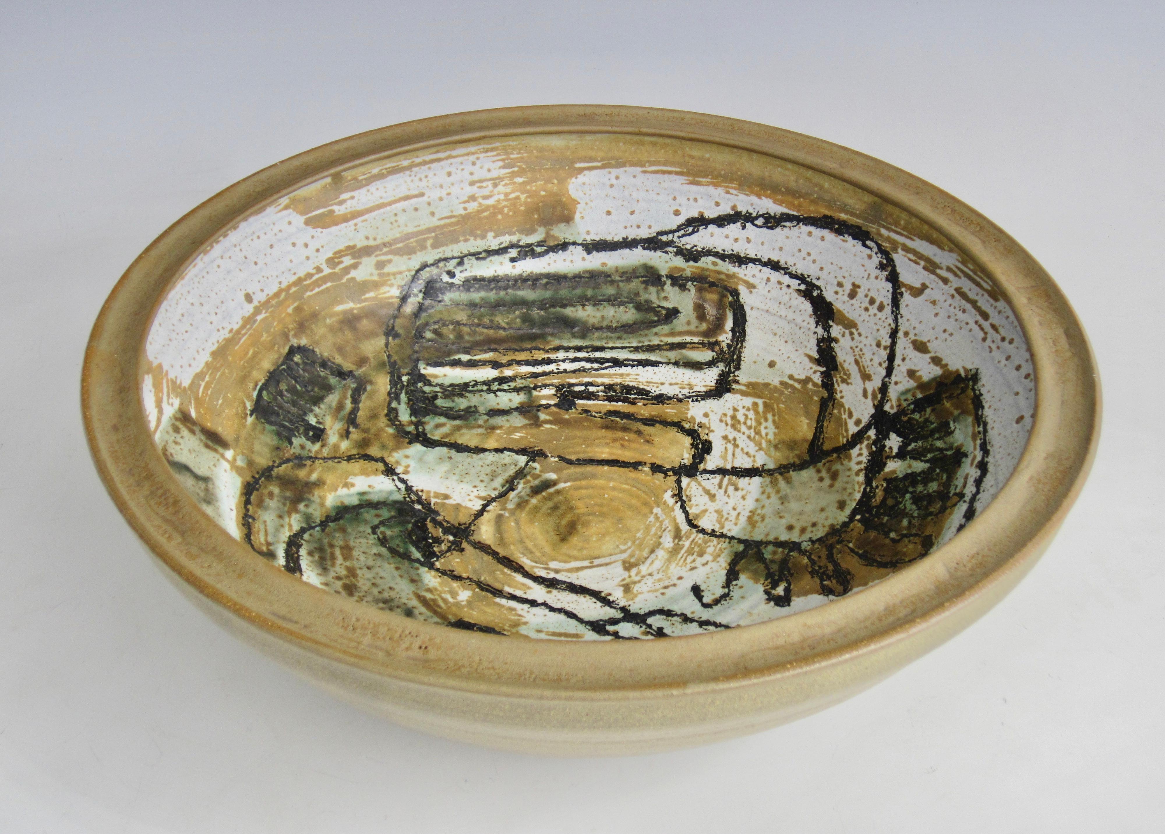 Artist signed and dated 1959, this large scale studio art earthenware bowl has approximately a one inch interior rim and khaki green exterior. Black lines and freeform shapes stand forward over washes of khaki, sage, and white on the interior. 
I