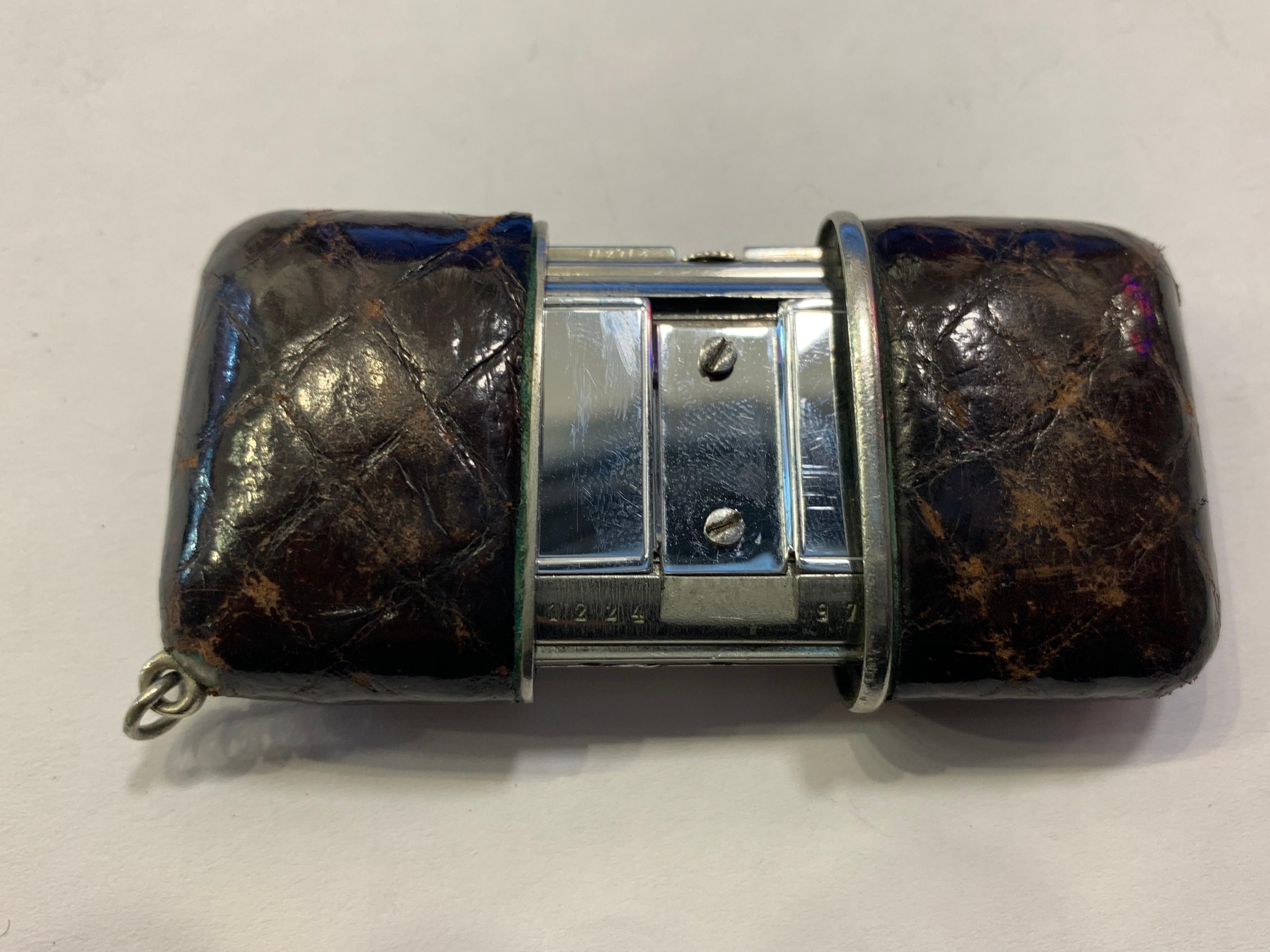 Eine silberne Movado 'Ermeto' Reiseuhr in einem braunen originalen Krokodilgehäuse. Das Zifferblatt ist mit 'Movado Chronometre Ermeto' signiert, die Zeiger sind aus blauem Stahl. Beim Öffnen der Schiebedeckel wird ein Ritzel auf der Aufzugswelle