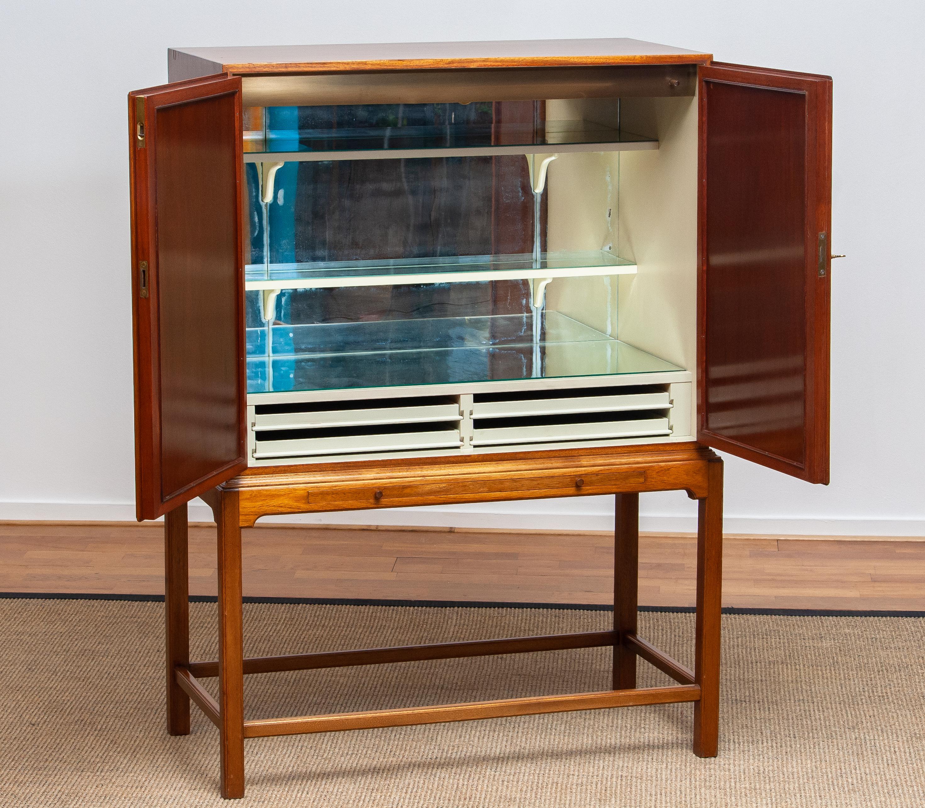 Beautiful dry bar / cabinet in mahogany on tall slim legs made in Sweden, 1950s.
Equipped with two lockable doors with behind four drawers and shelves. The shelves and rear are decorated with glass mirrors. Also an extendable shelf at the front