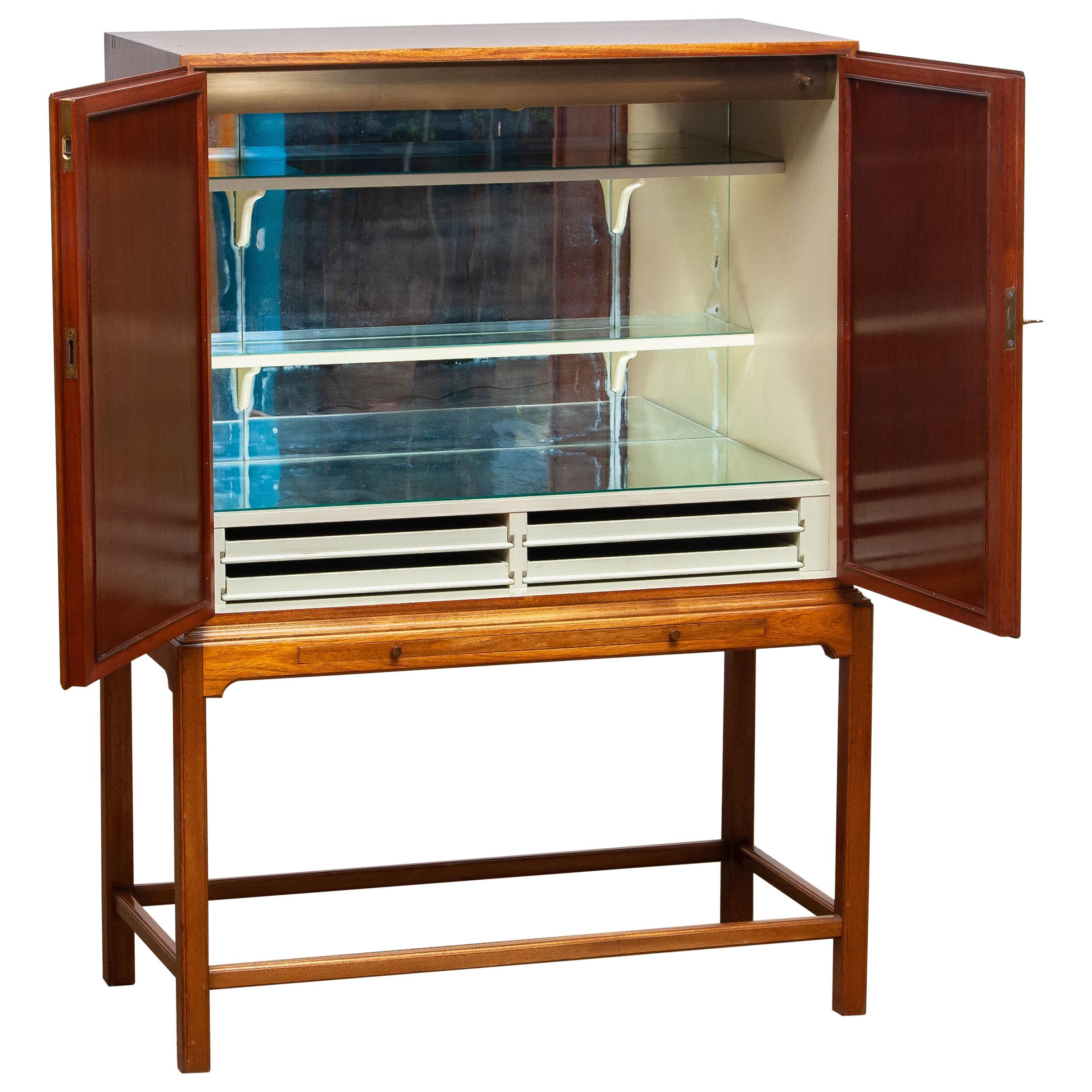 Beautiful dry bar / cabinet in mahogany on tall slim legs made in Sweden, 1950s.
Equipped with two lockable doors with behind four drawers and shelves. The shelves and rear are decorated with glass mirrors. Also an extendable shelf at the front