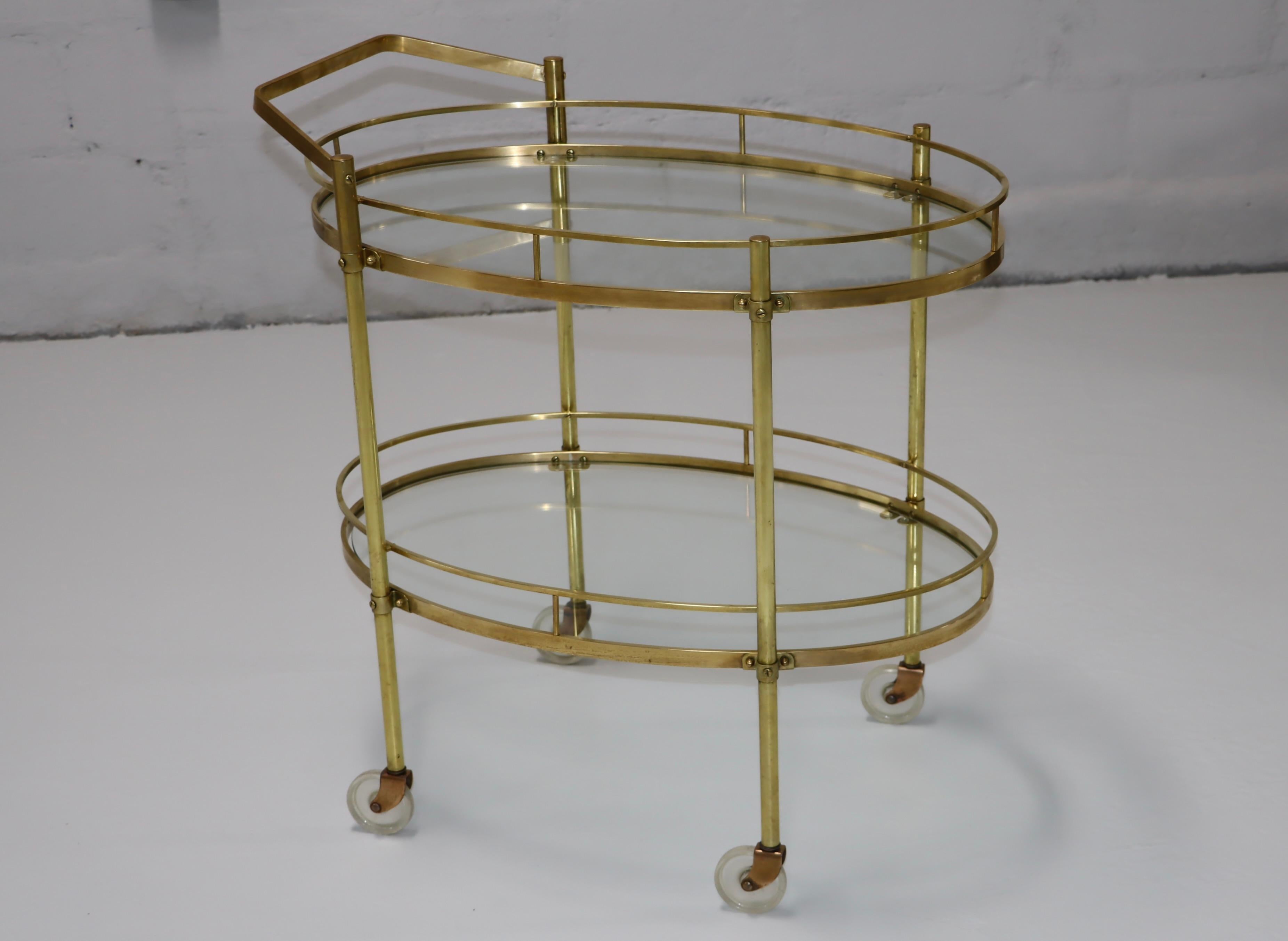 1950's solid brass Italian two tier oval bar cart with removable handle and glass shelves, lightly hand polished with some wear and patina to the brass due to age and use.