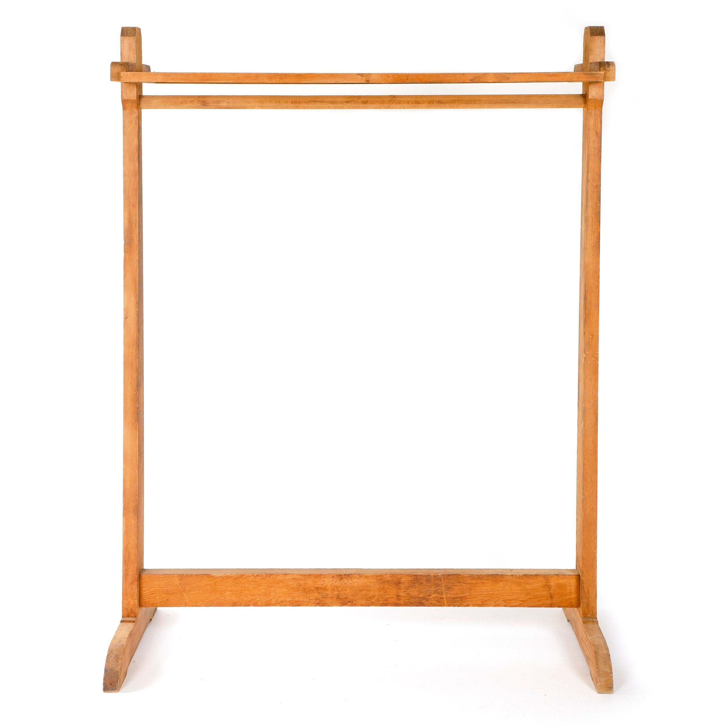 A simple, sturdy, and well made utilitarian clothing rack of solid pine set on a shoe foot base. The thick upright stiles form supporting sides for a slatted rack, a shaped pole for hanging articles, and a lower stretcher nicely tenoned through the