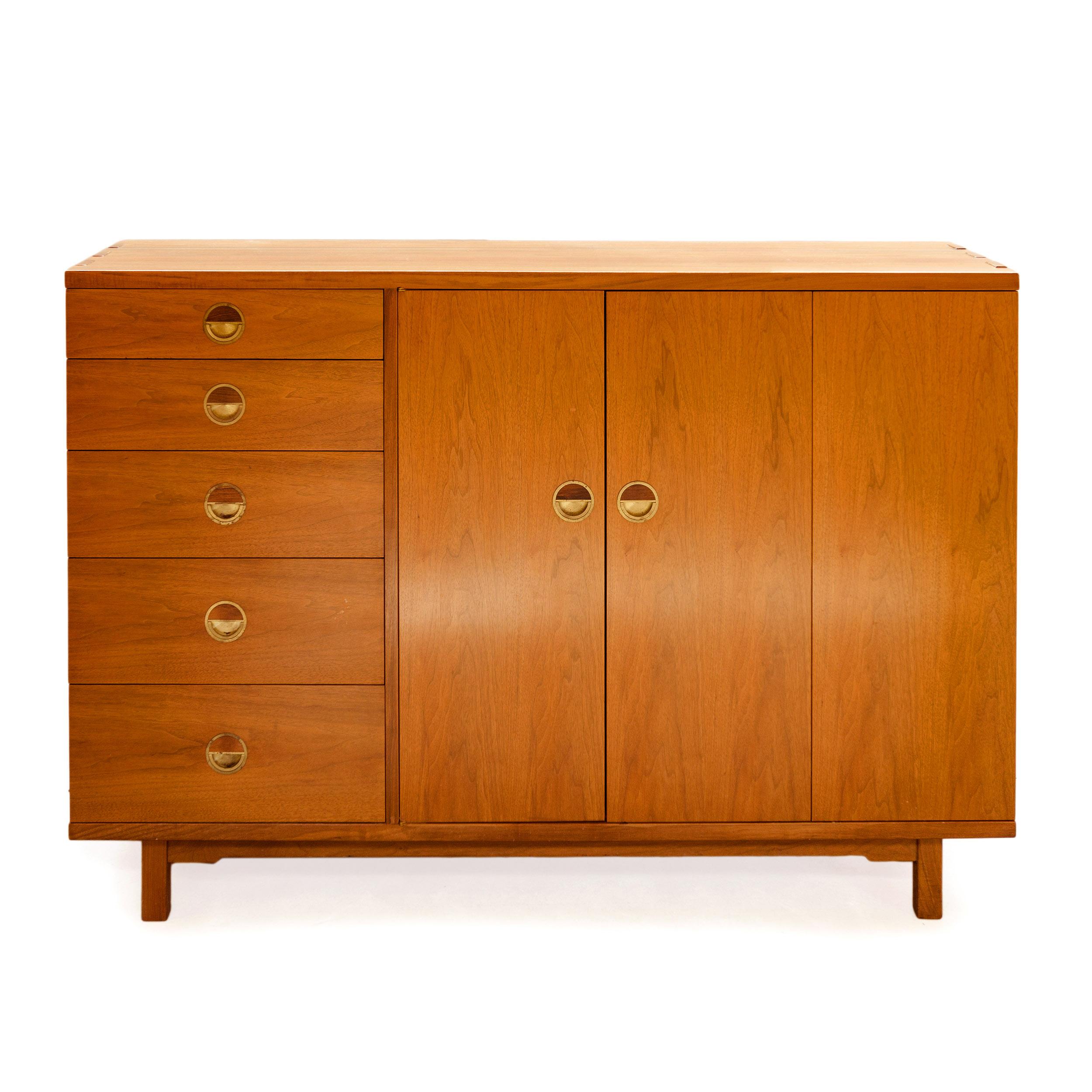 An asymmetrical dresser in solid walnut with exposed finger jointed joinery, having a shelved compartment accessed by bi-fold doors flanked by a bank of five drawers with exquisite brass hinged ring pulls inset with rosewood.