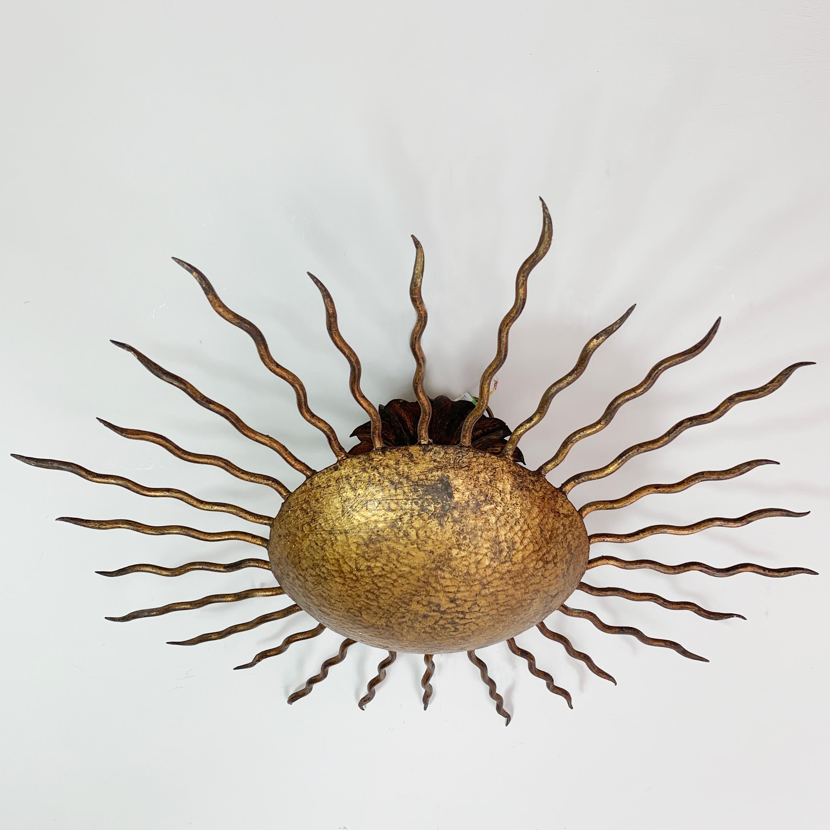 Spanish sunburst ceiling light,
circa 1950s
Hand forged metal sunburst with gilt finish
Spikey gilt rays emit from the central hammered metal disk
Measures: 55 cm width, 15 cm depth
The light takes 2 x E14 screw in bulbs

There is a ceiling