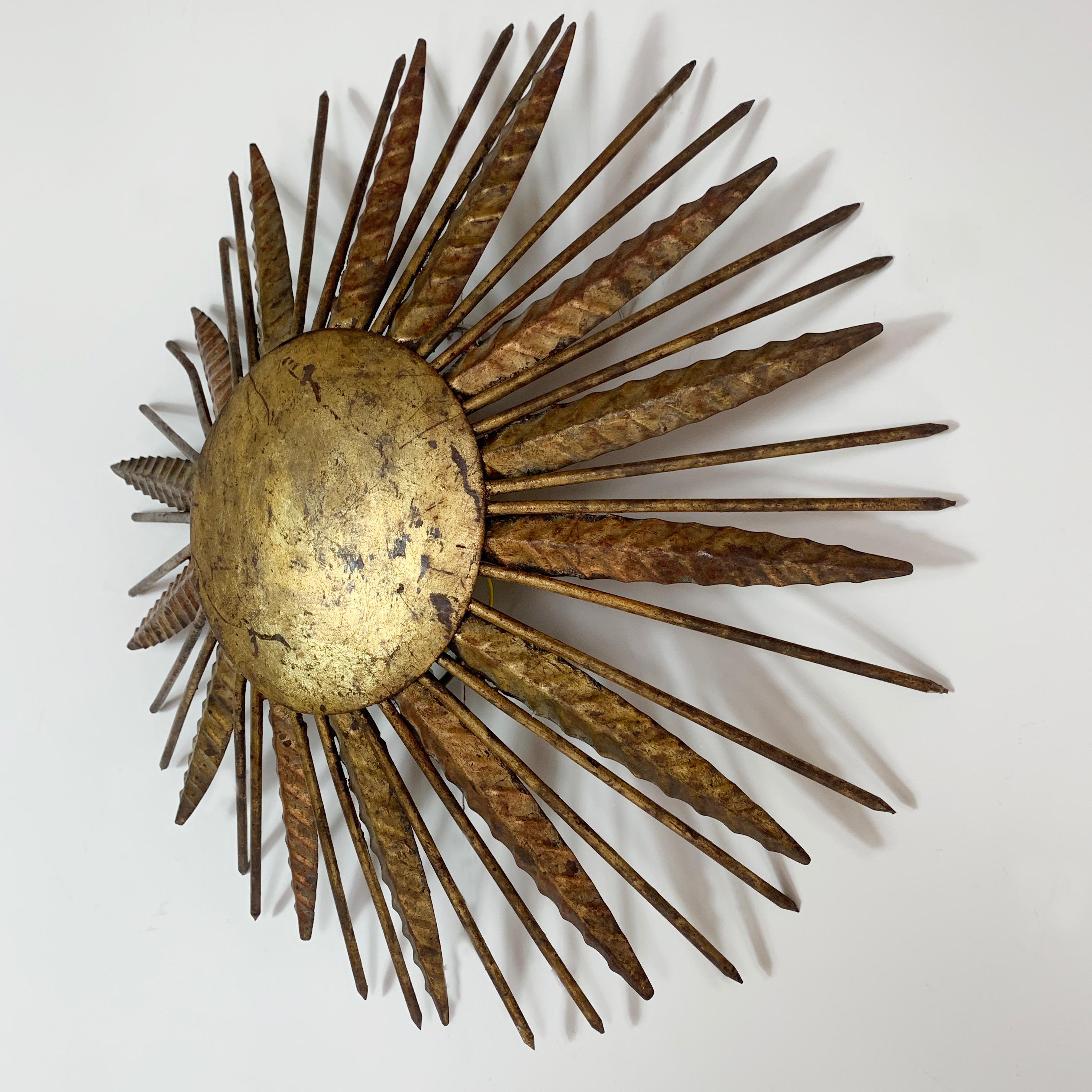 Spanish sunburst ceiling light
circa 1950s
Hand forged metal sunburst with gilt finish
Measures: 50cm width, 11cm depth
Spikey gilt nail rays emit from the central disk
The light takes 2 x E14 screw in bulbs
There is a hanging hook on the back