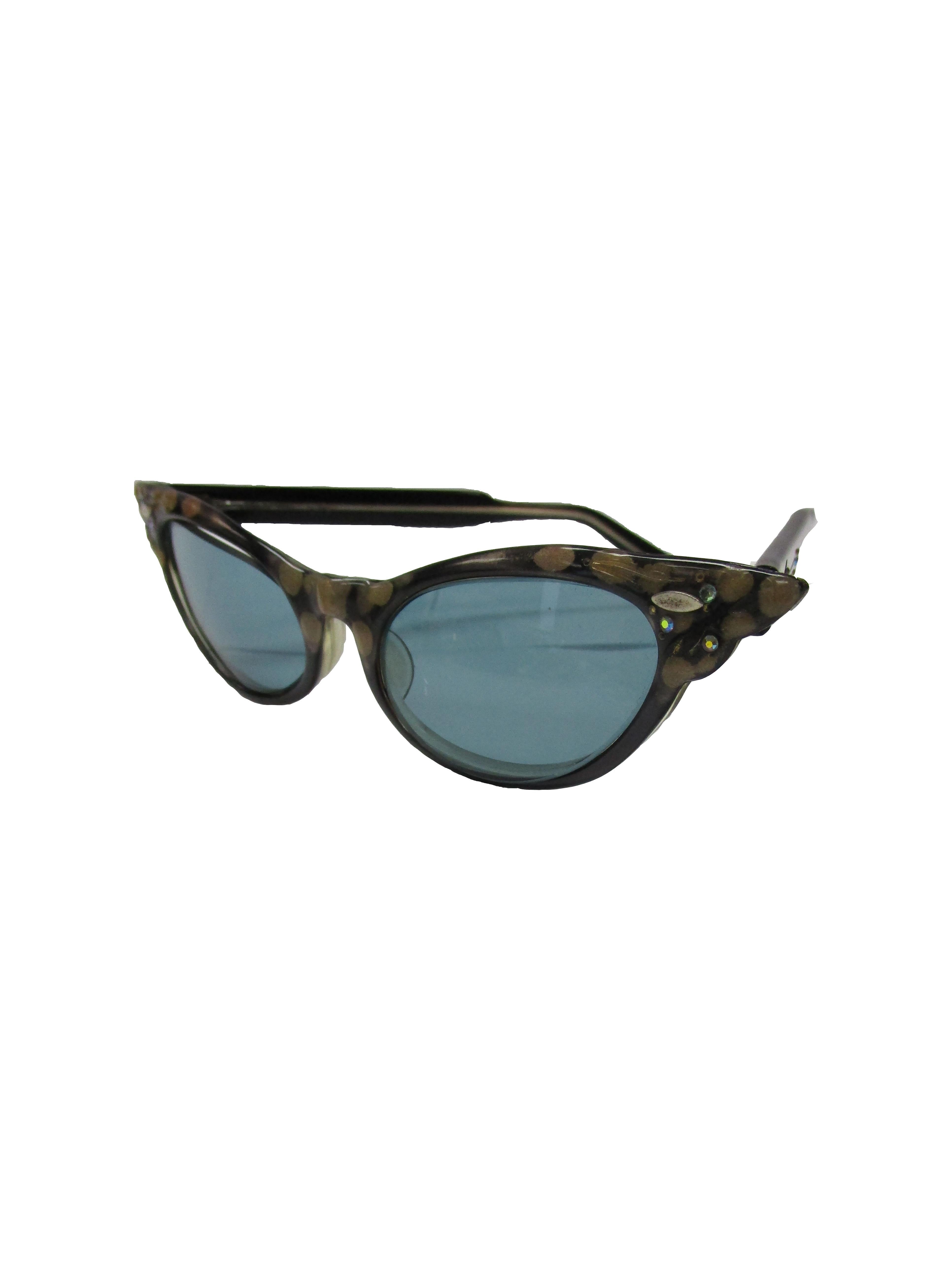 

 Effortlessly cool sunglasses from the 50s. Featuring a black and brown spotted frame with grey tint lenses which complement the glasses well and provide contrast. Jeweled details can be found on the side of the arms and on the frame's corners