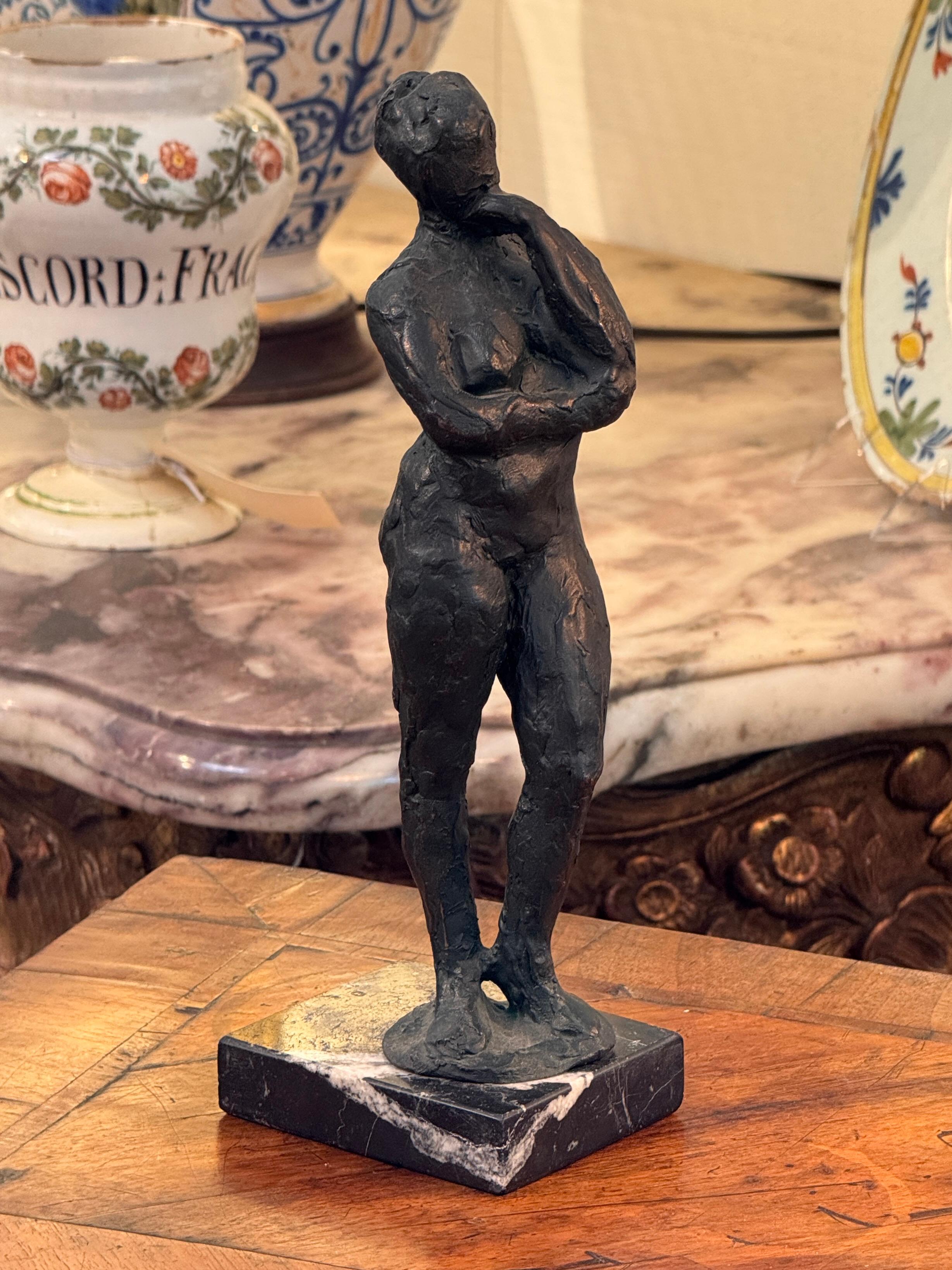 Expresiva escultura de fundición de un desnudo femenino de pie en pose contemplativa. La superficie está modelada toscamente con un acabado orgánico y texturizado, que capta el movimiento y la forma en un lenguaje modernista. Montada sobre una base