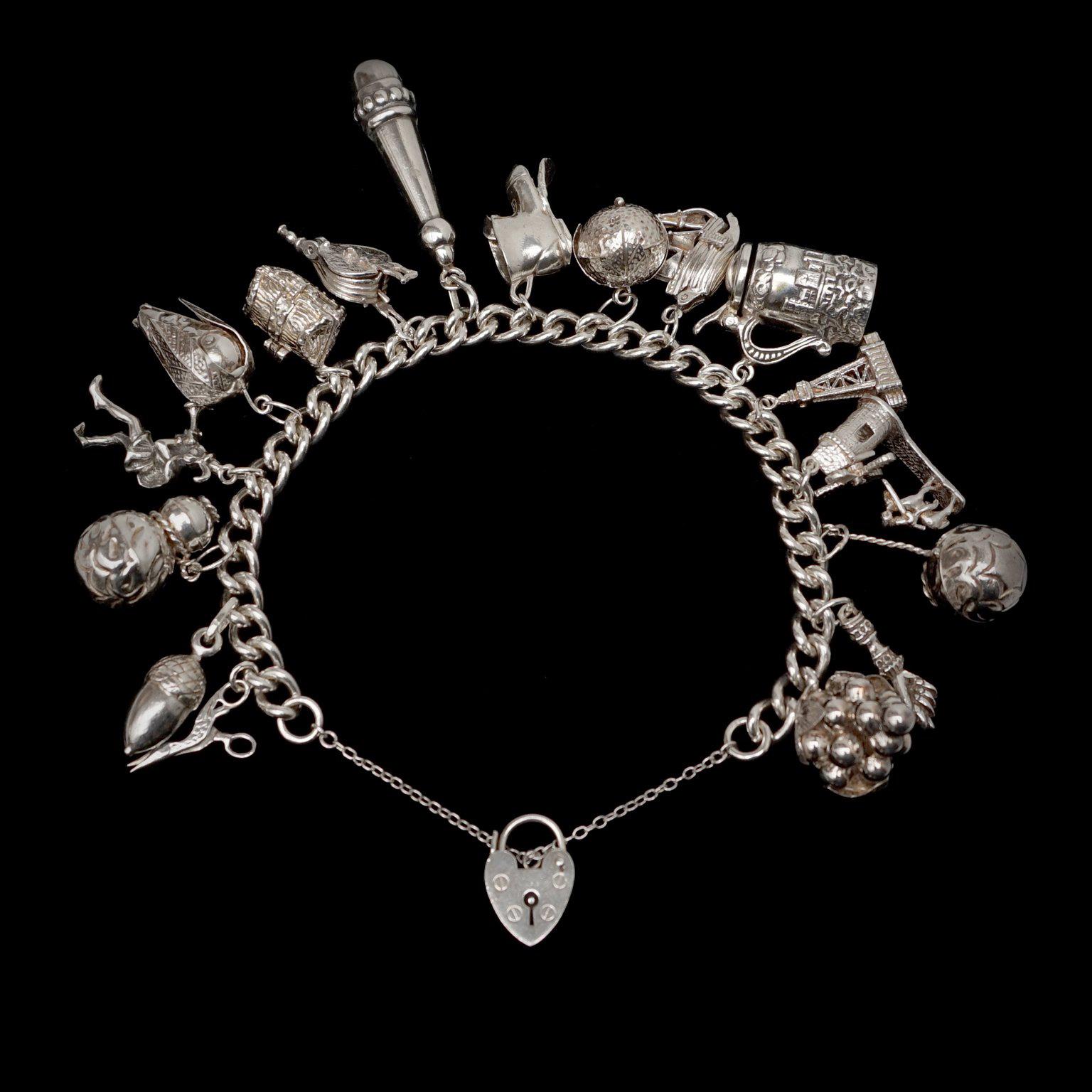 This English 1950s heavy sterling silver bracelet has 17 large three-dimensional charms and opens or closes with a heart shaped padlock on a little safety chain.

Some of the charms have moving or opening parts. 
The windmill really turns, the